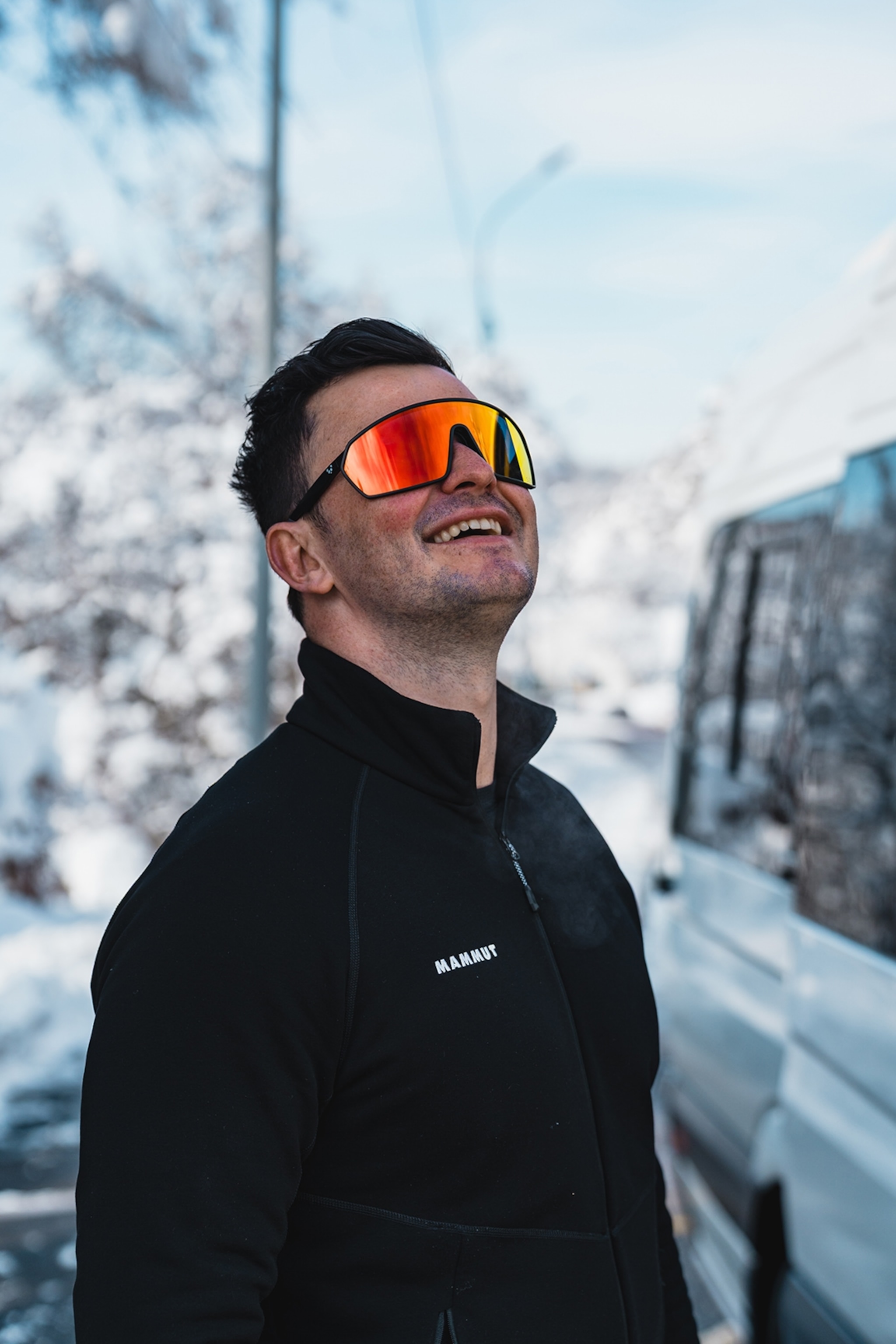 A snowboarder looking up at a mountain with his glasses on.