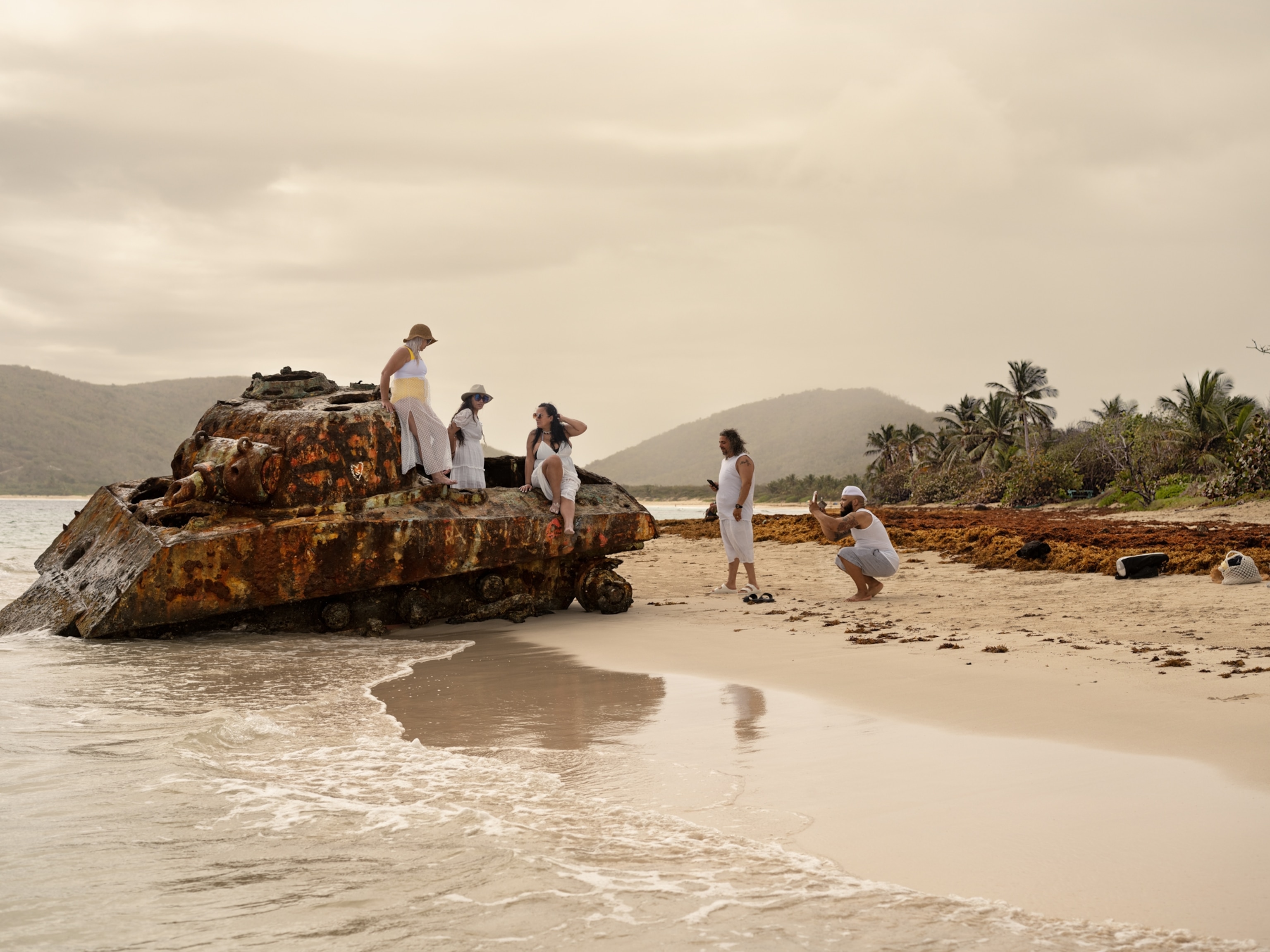 Group of people posing on the rusty tank on the shore.