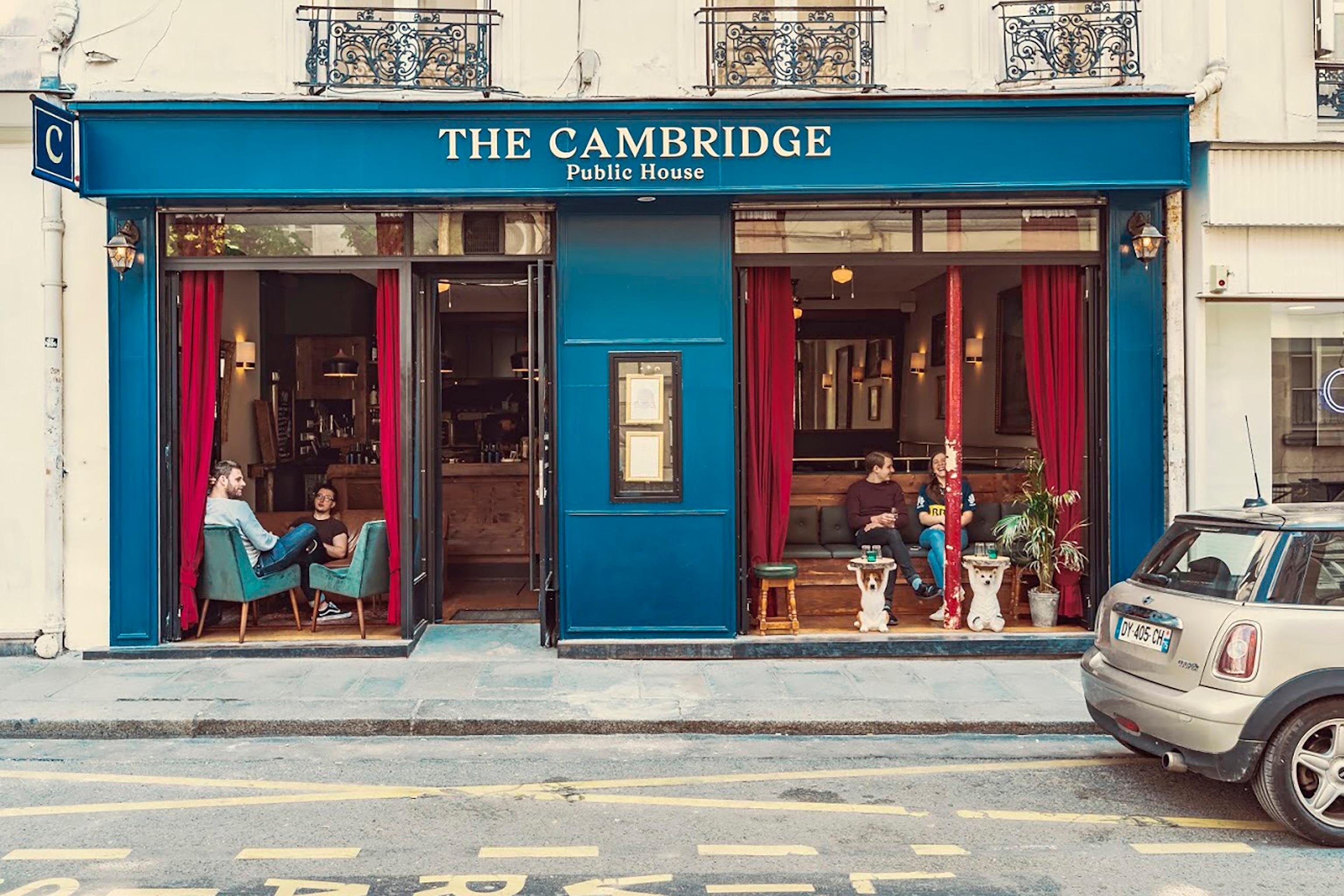 The facade of an old-timey pub in Paris, with floor to ceiling windows that open onto the sidewalk.