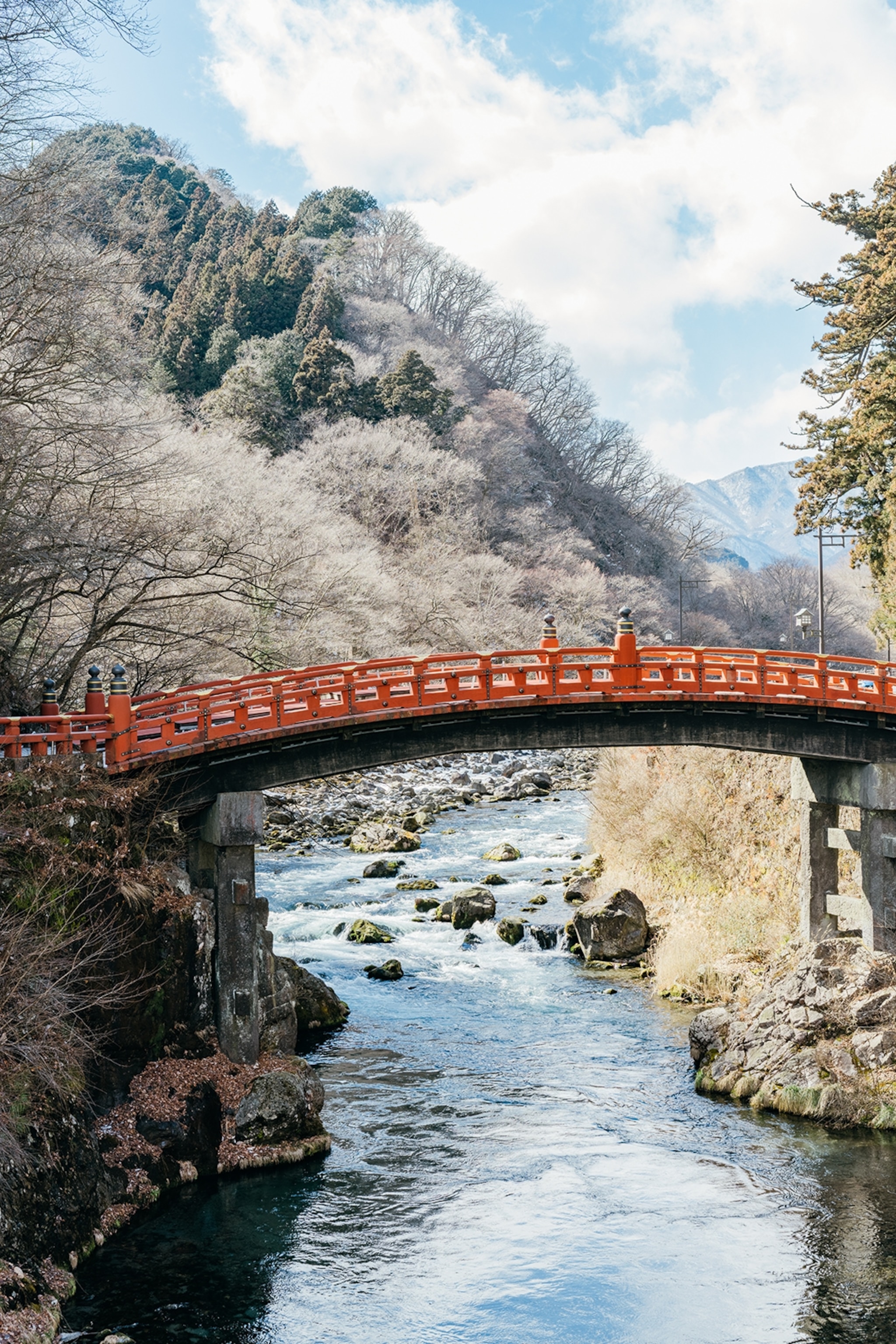 An arched bridge leading over a coursing river with a frosty mountain landscape in the background.