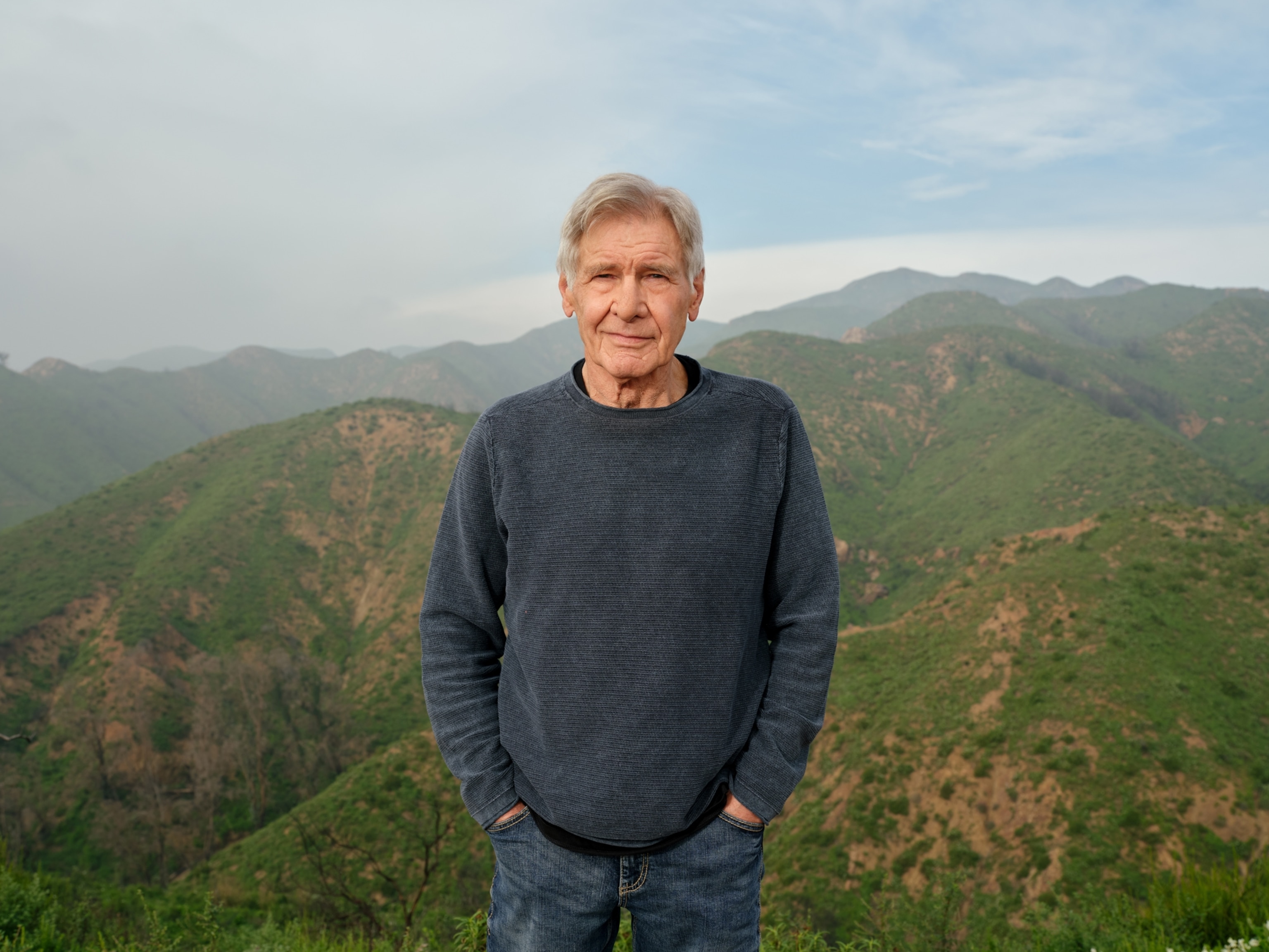 A man stands in front of mountains on a clear day.