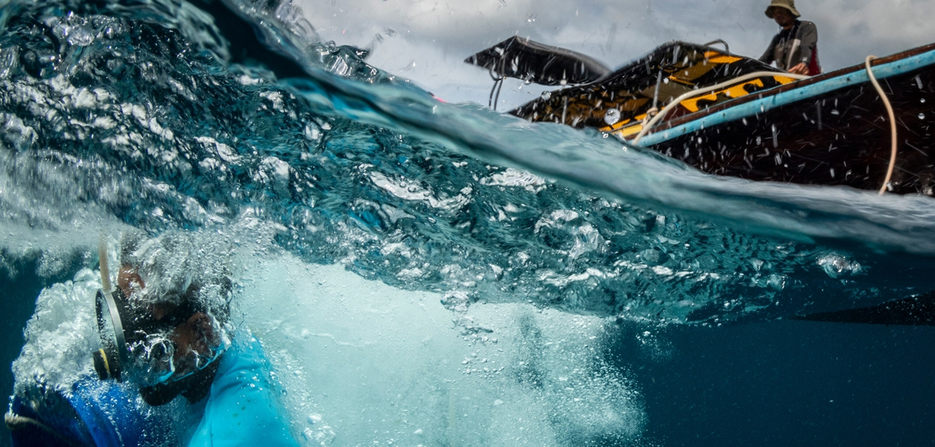 Image of Urak Lawoi fisherman in the sea with homemade compressor diving equipment while fish handler looks on from longtail boat.