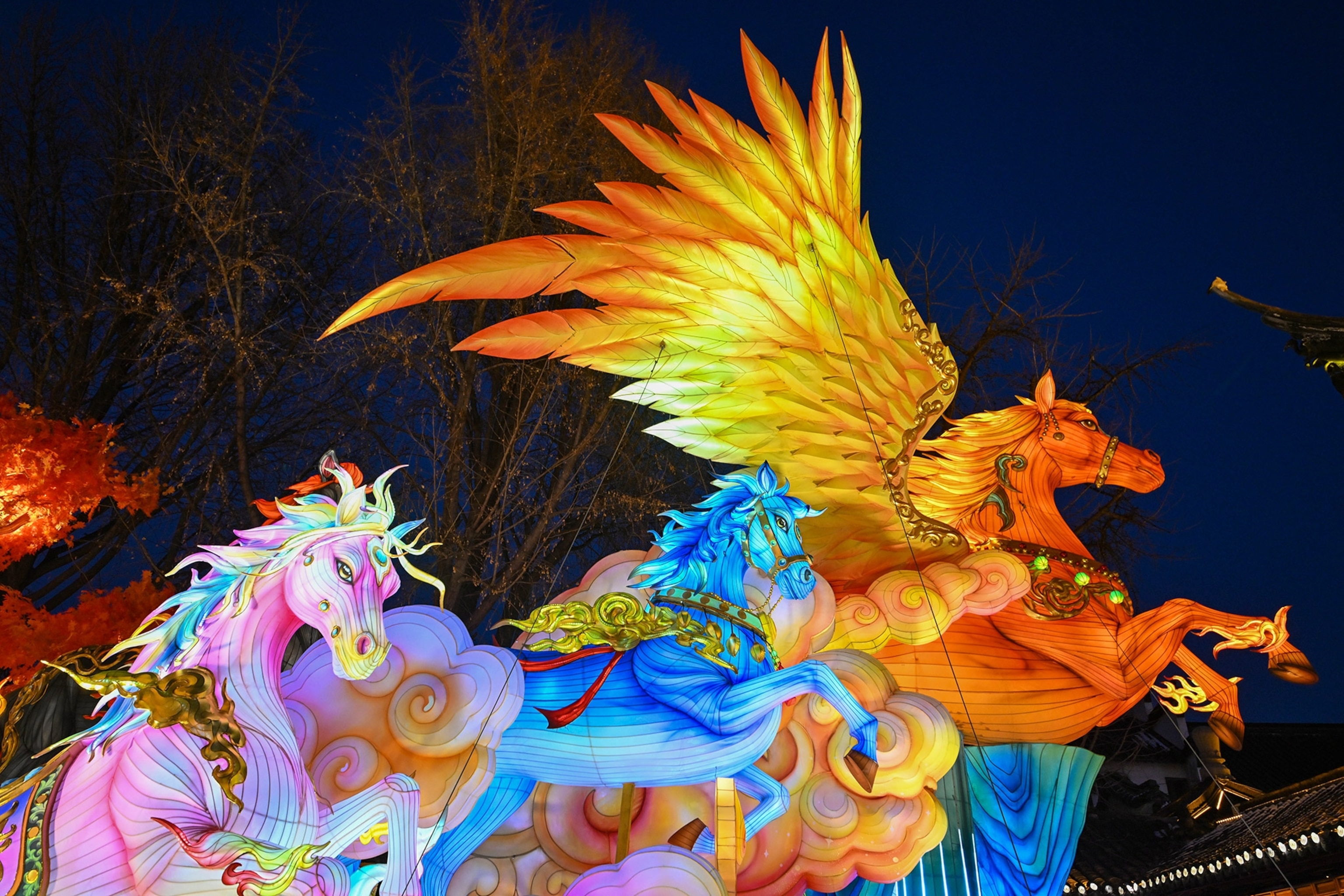 Brightly lit, colorful figures of three winged horses rearing up against a black sky