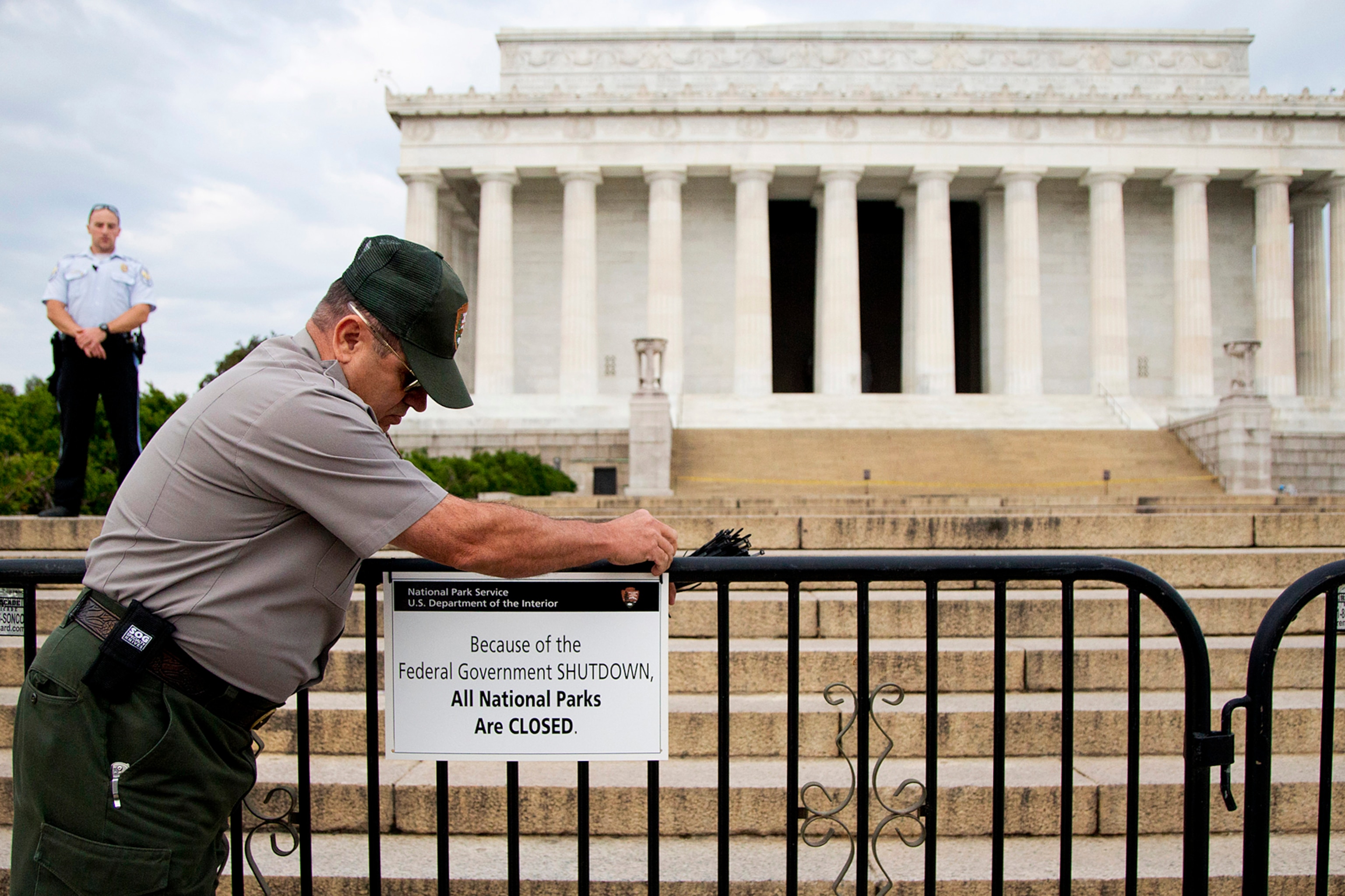 A US Park Police officer watches at left as a National Park Service employee posts a sign on a barricade closing access to the Lincoln Memorial in Washington, Tuesday, Oct. 1, 2013, thanks to the US Government shutdown.