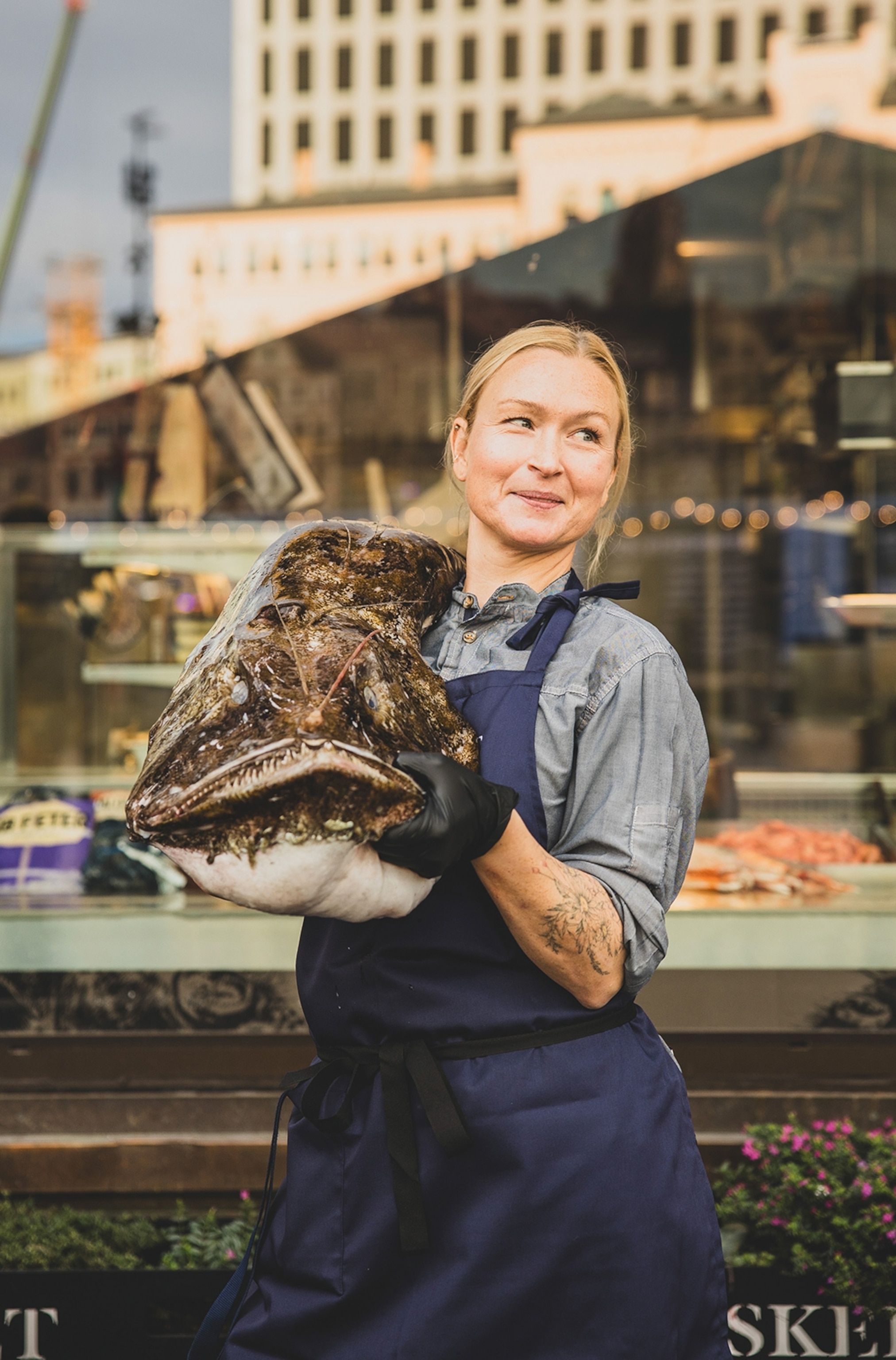 Fishmonger outside a shop holding a big monkfish.