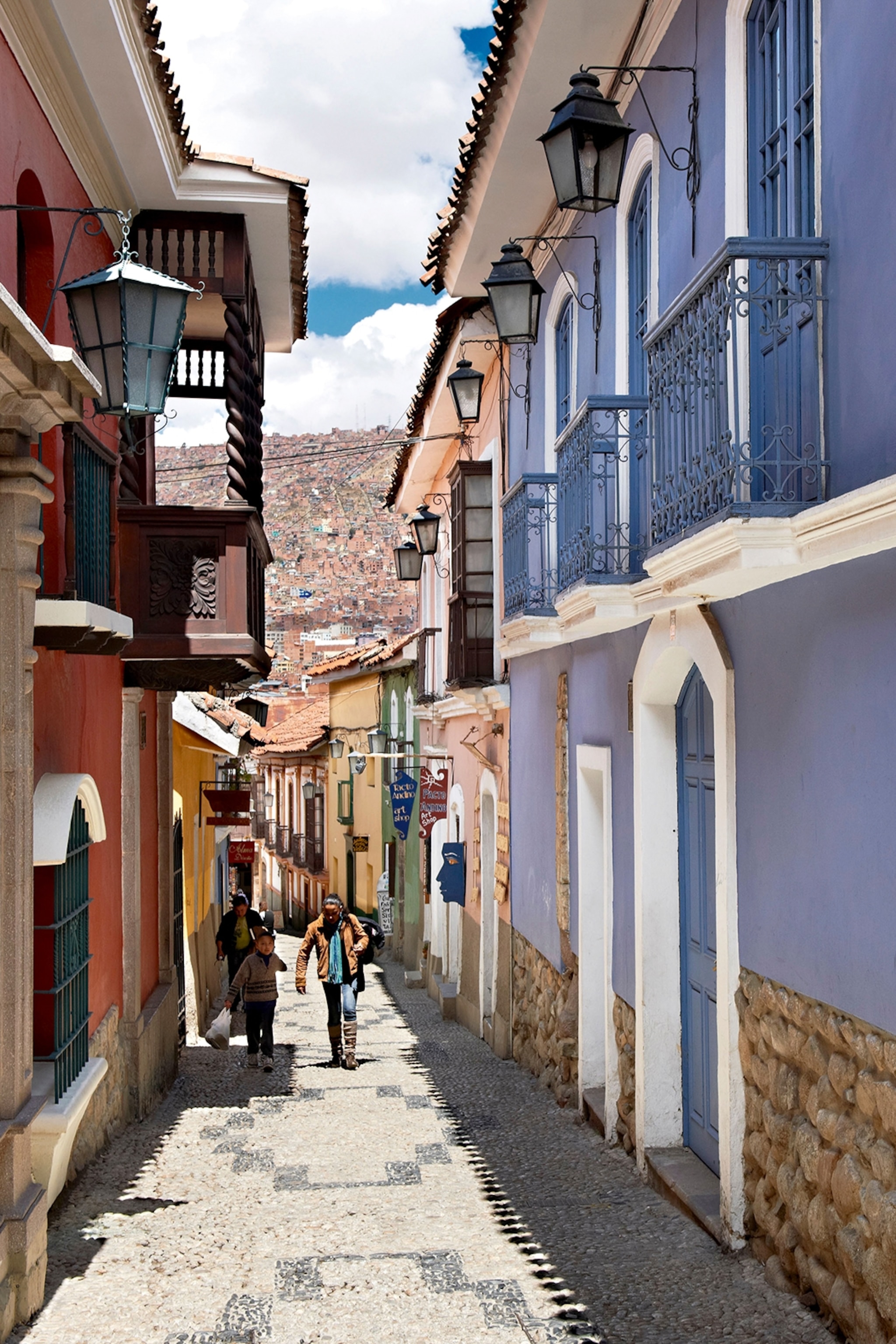 A downhill street view of narrow alleyway between colonial-style, residential houses with lanterns.