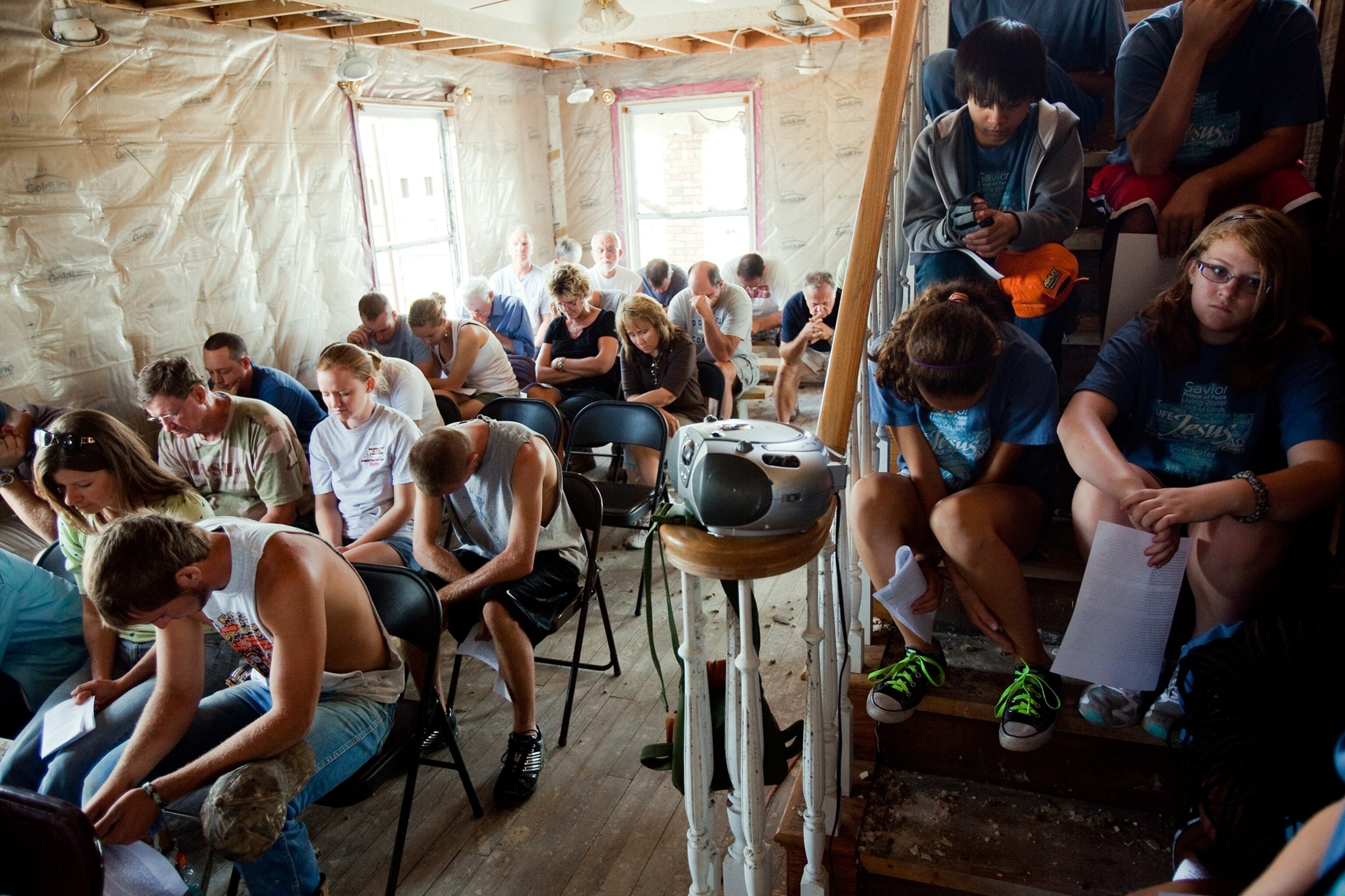 How Joplin Recovered - A group of people sit praying in a church under repair.