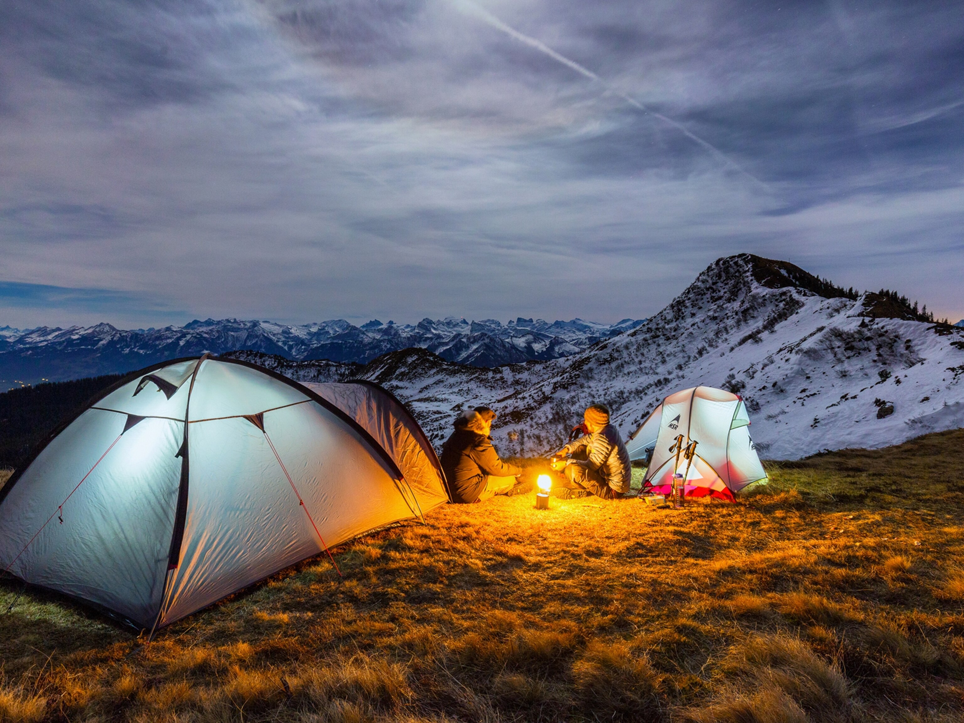 two people camping out in tents by a camp fire near the Swiss Alps