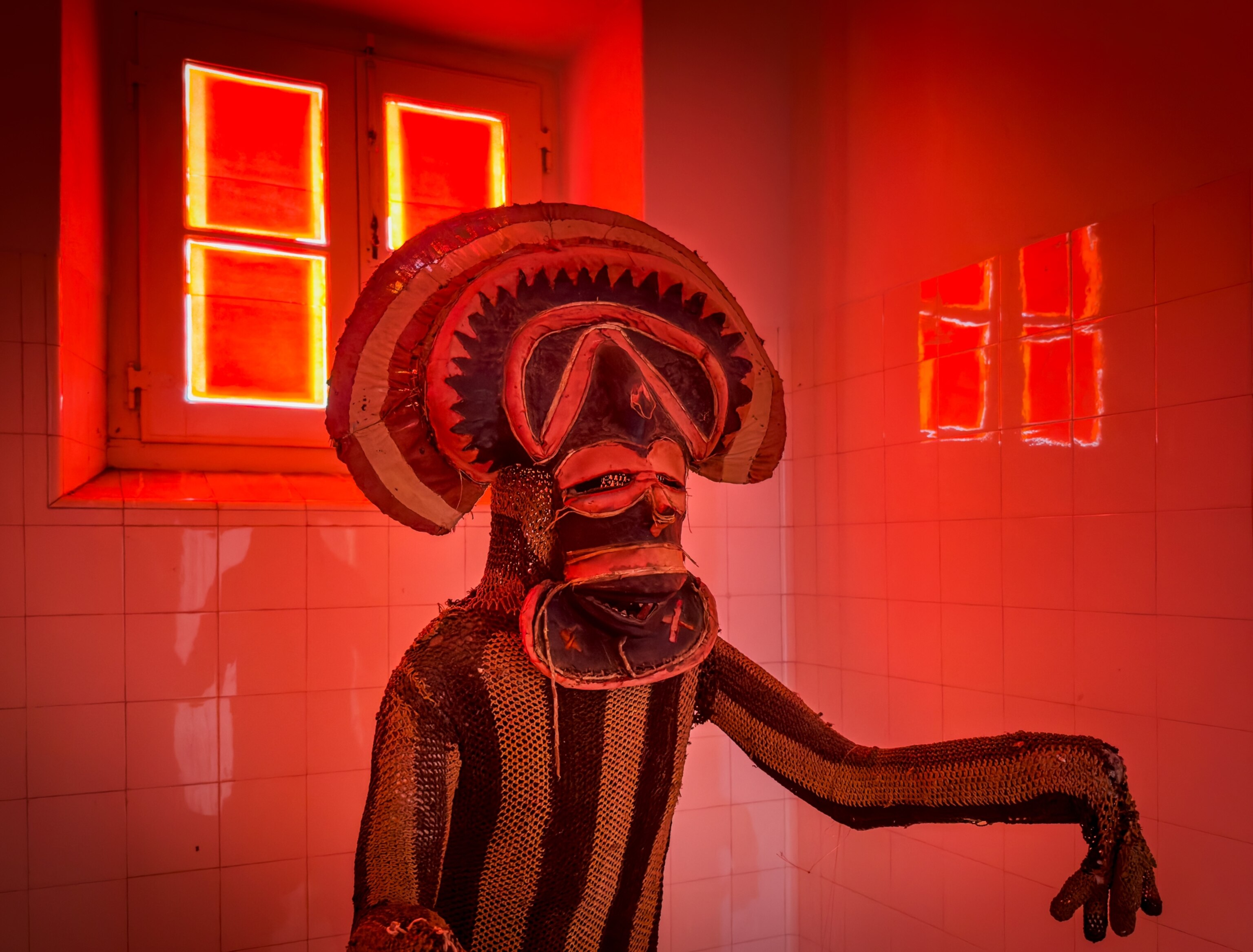 Museum display figure dressed in traditional costume and mask in red light.