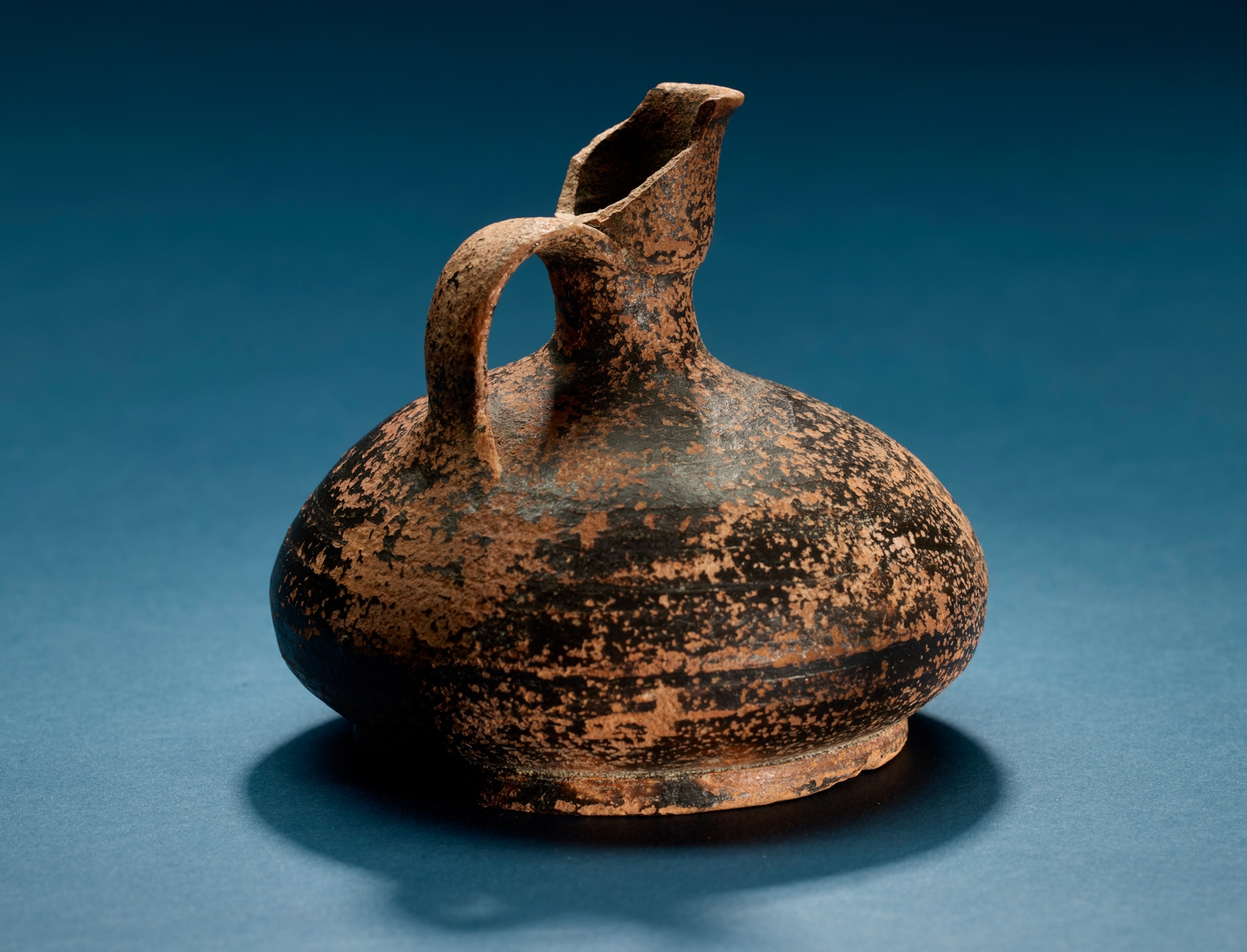 Glazed ceramic pitcher or jug, rounded body with vertical flared spout at top attached to loop handle, short footed base.