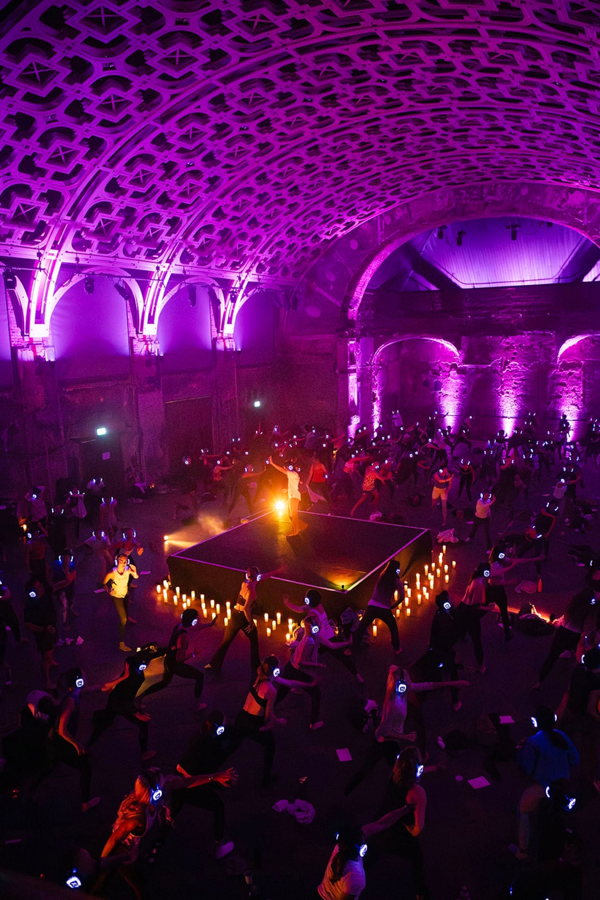 A hall lit only with LED light with a platform in the center and people dancing around it.