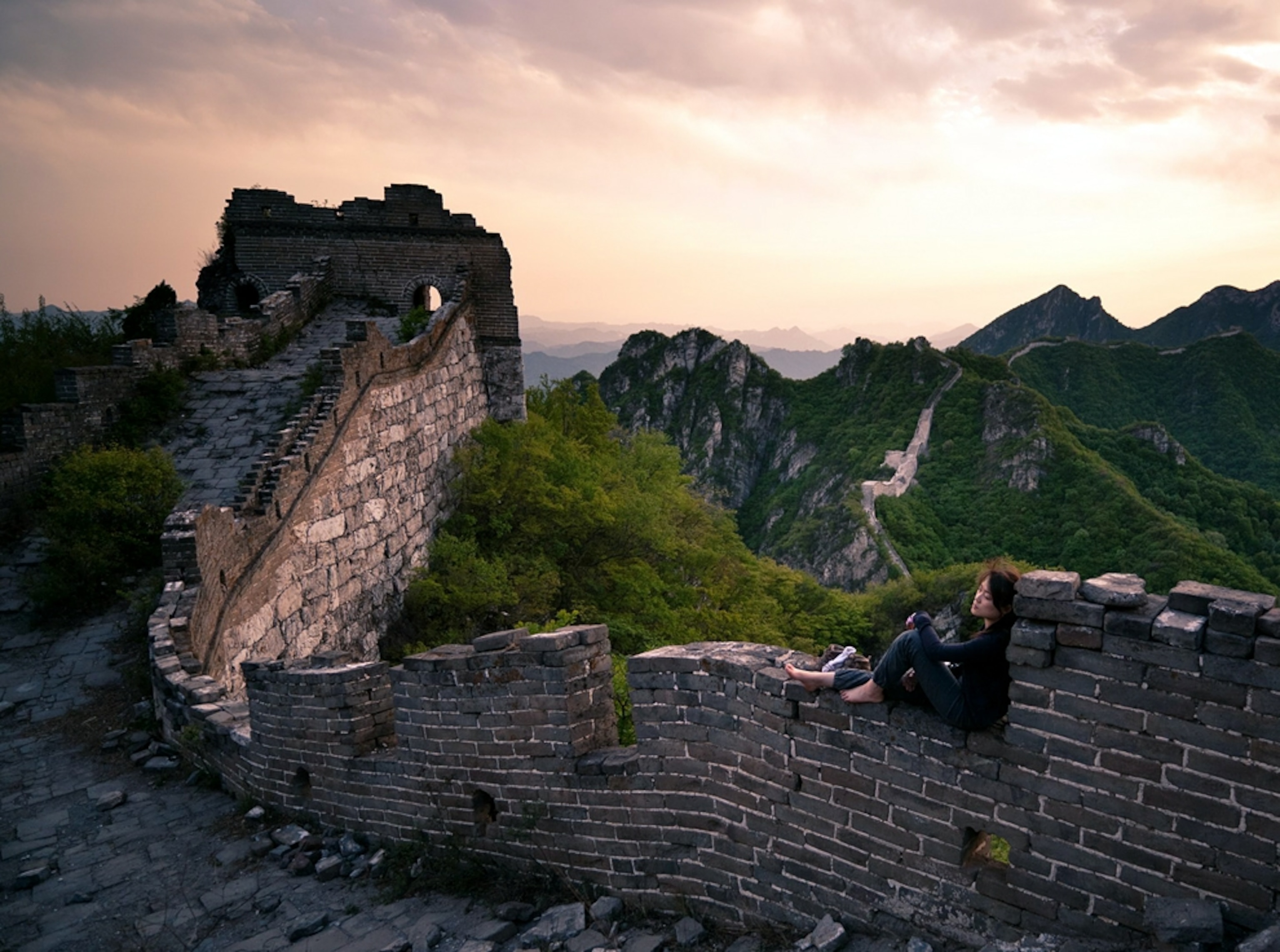 Woman rests on top of the Great Wall of China at dusk
