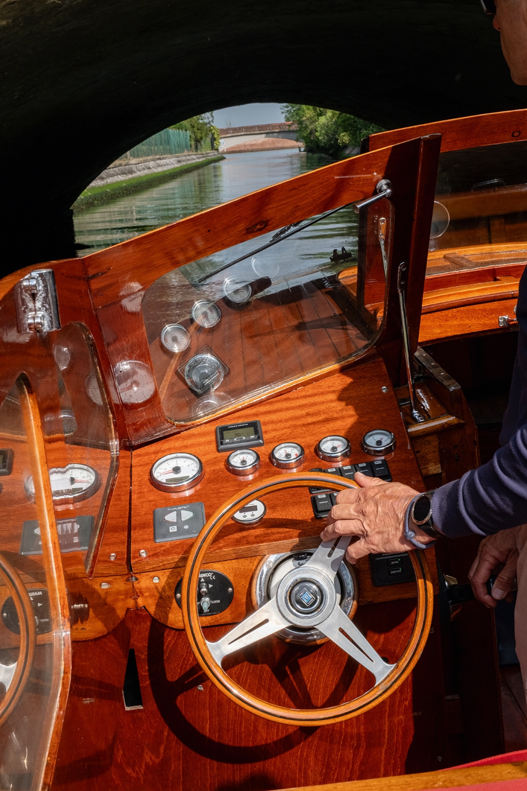 Close-up on the steering wheel of a vintage mahogany motorboat with one hand on the wheel.