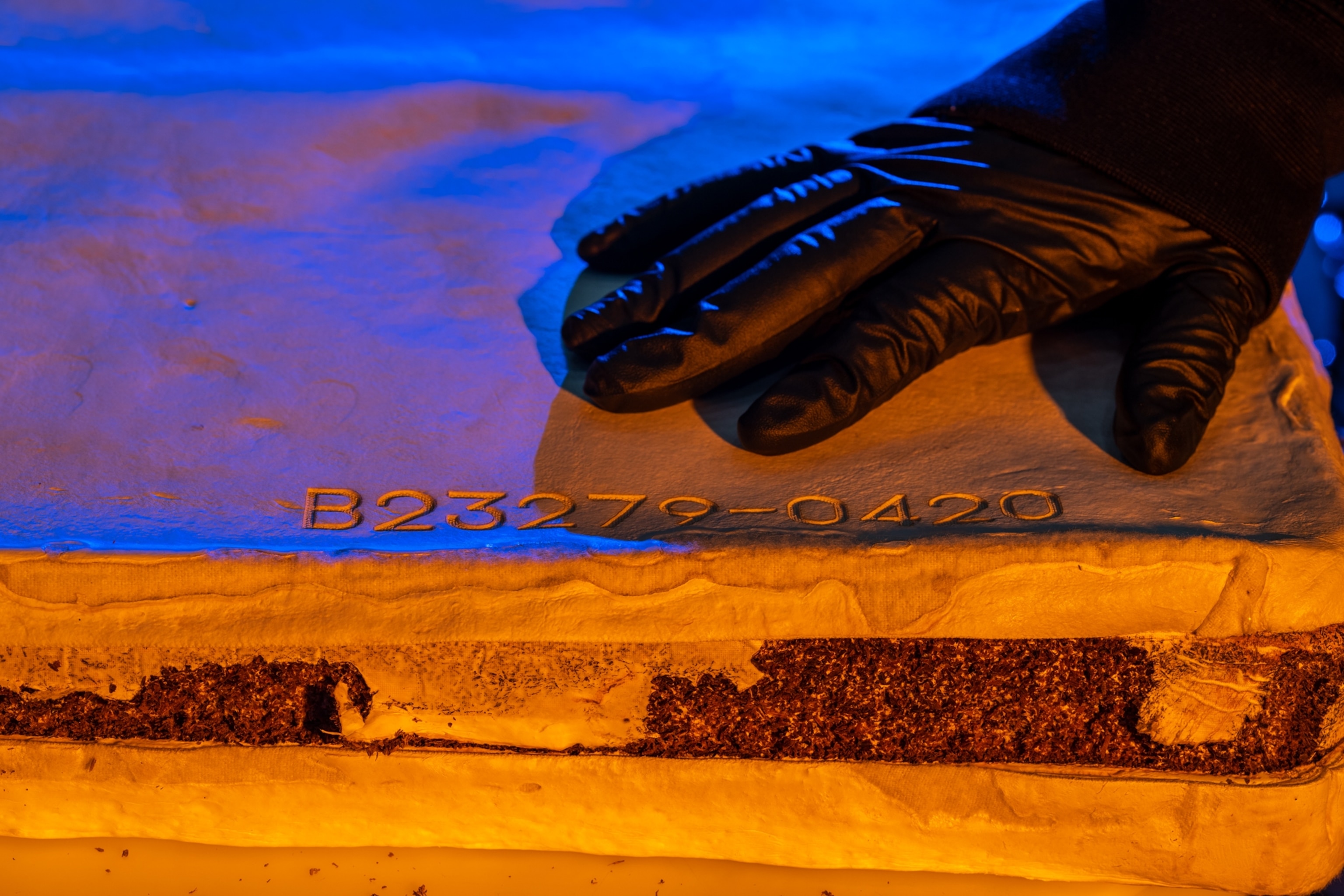 Hand in black glove holding down what looks like a sandwich.