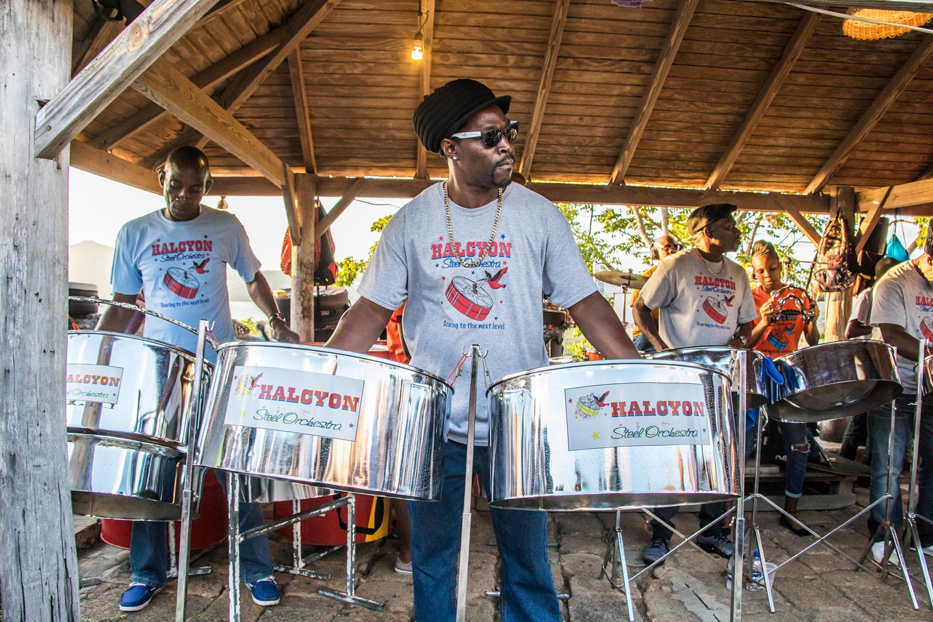 A group of people, one man in central foreground, gathered behind large silver steel drums under an overhang