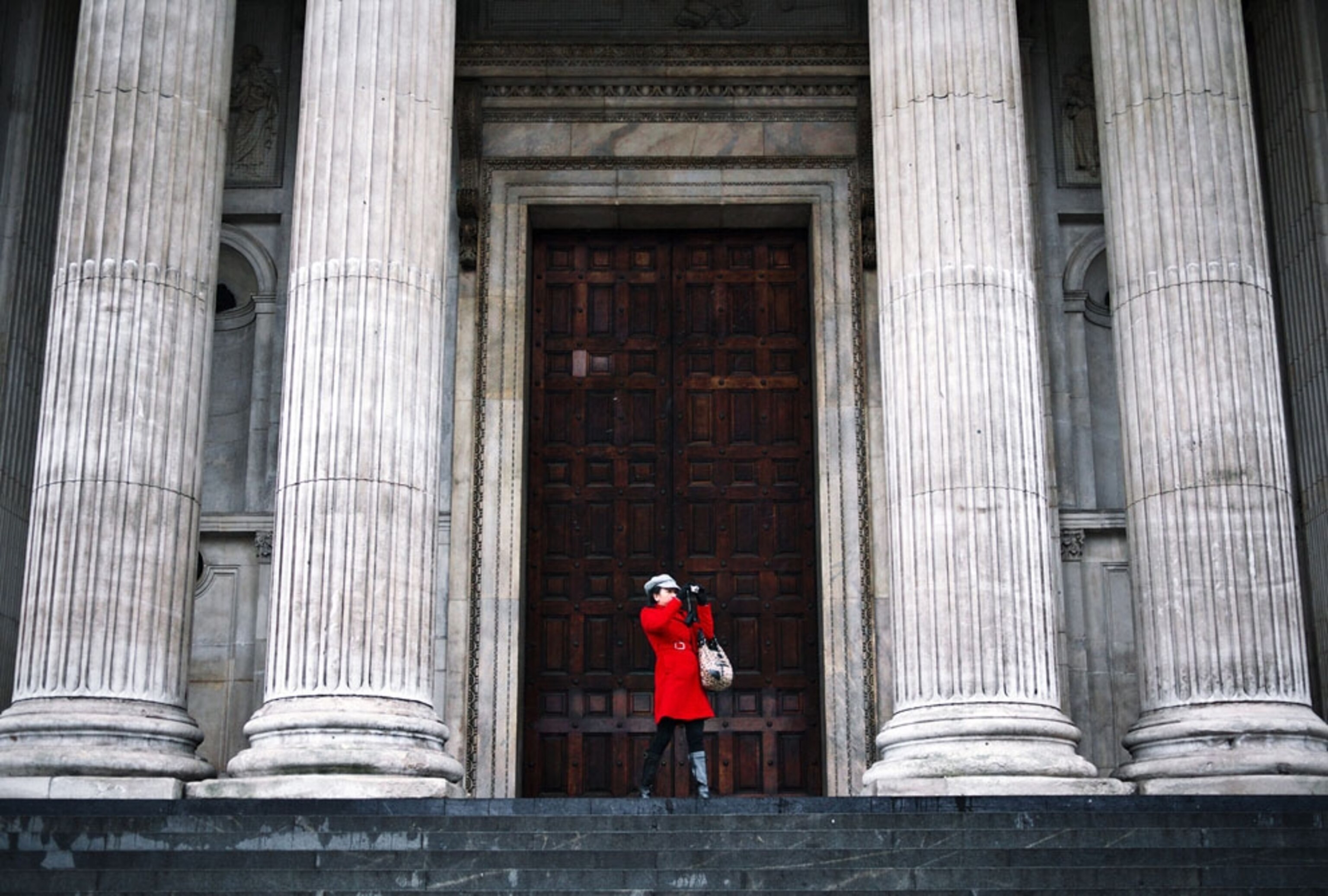 A woman in a red coat photographing the columns of St. Paul's Cathedral, London