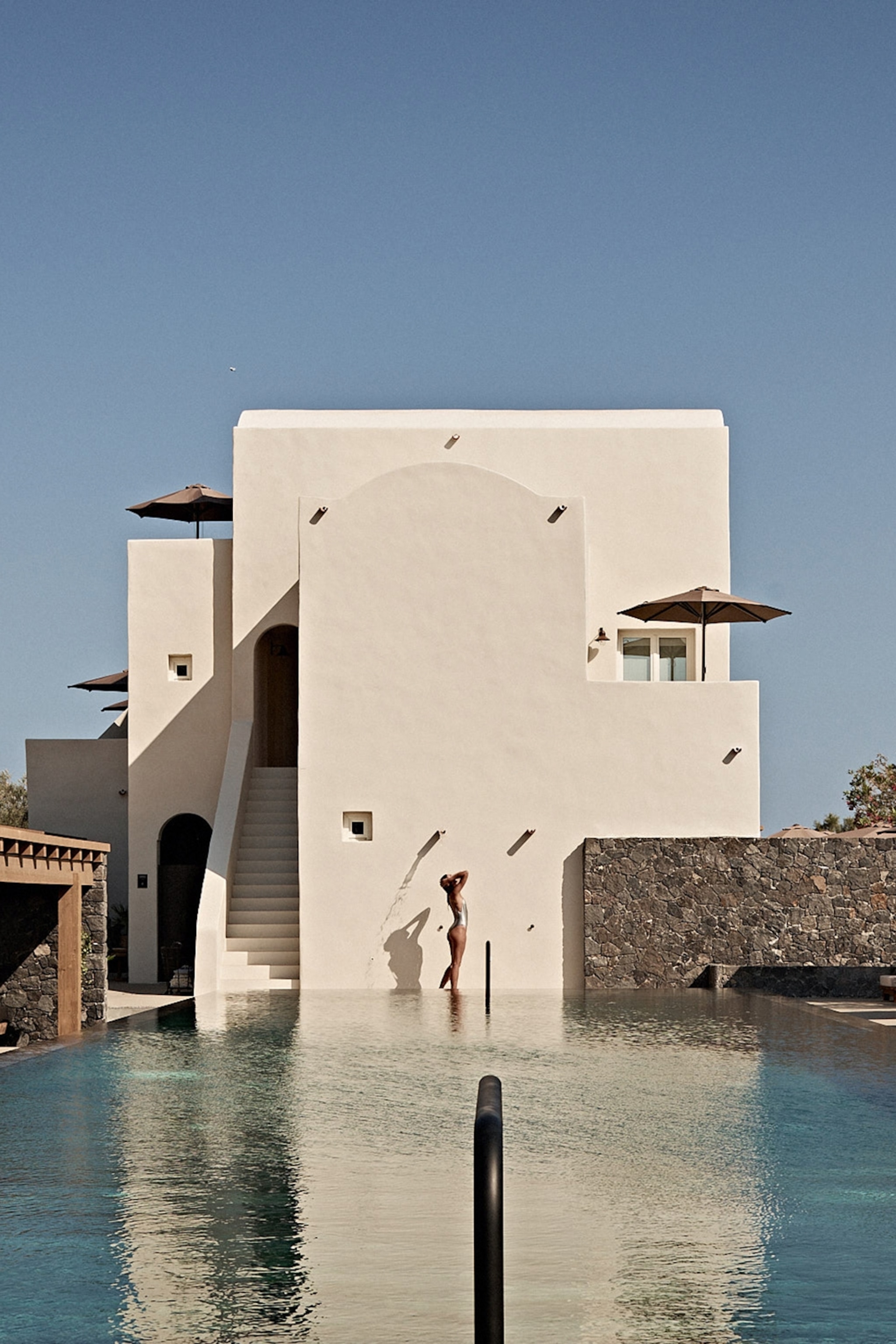 A wide pool in front of a sleek, stone house.