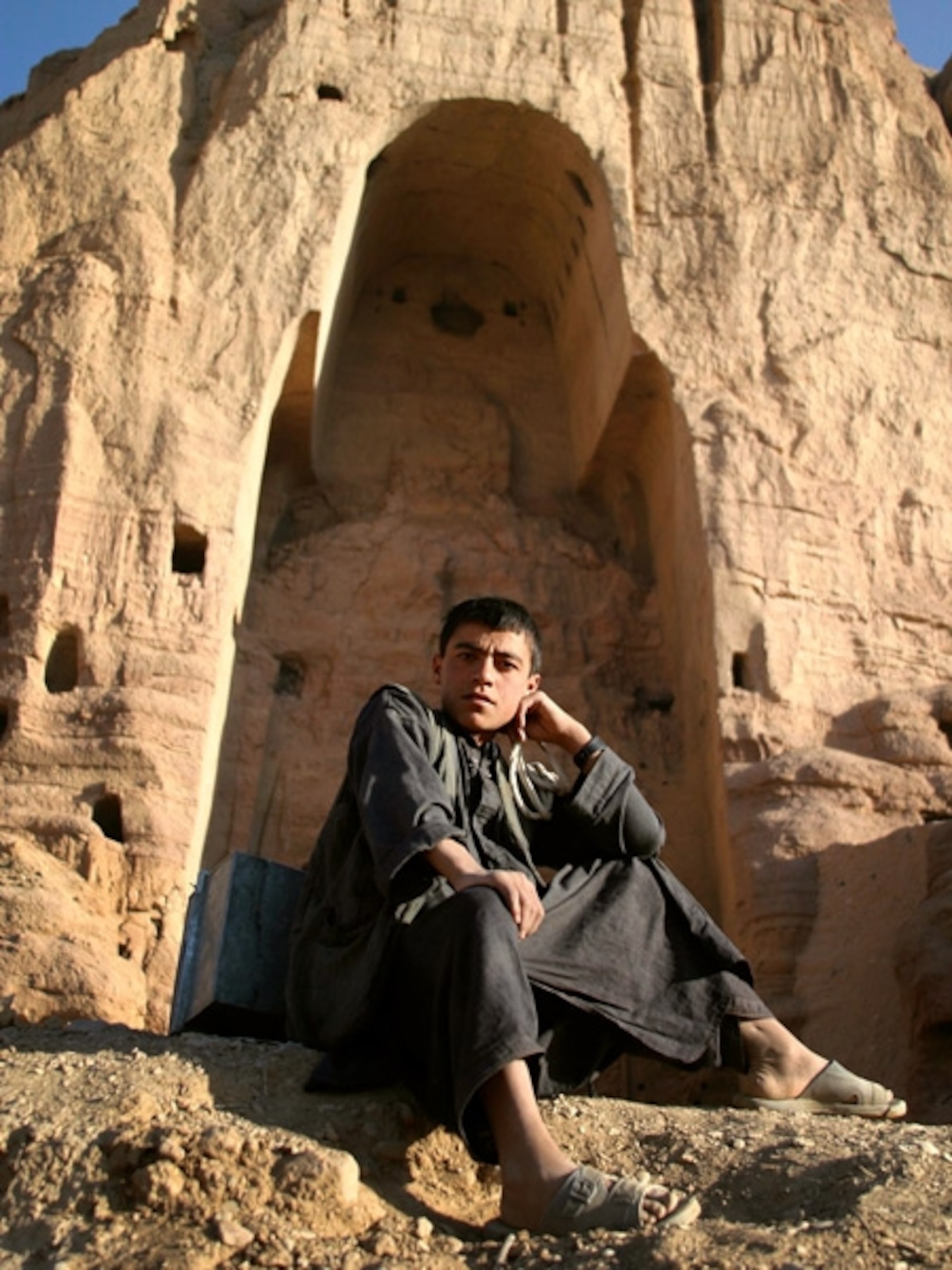 A boy sitting in front of a carved out cliff