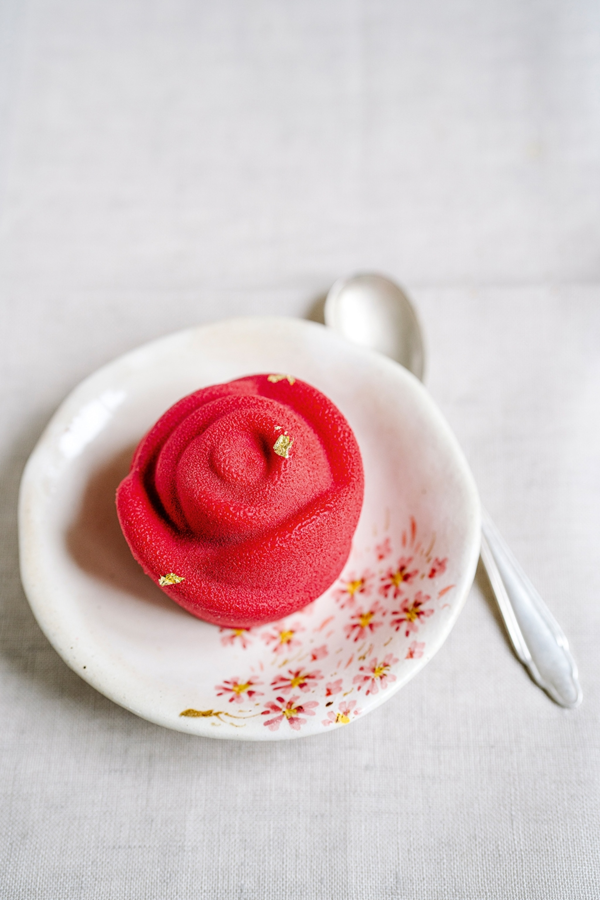 A ceramic plate with sakura blossoms painted on and a tarte with a smoothed over, rose-like topping and gold-leaf.