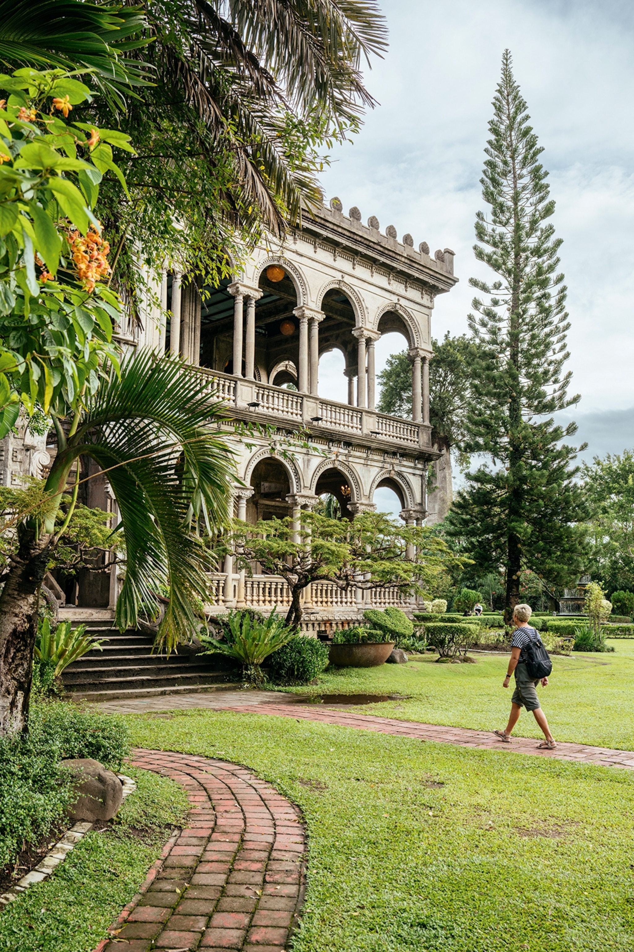 The exteriors of a mansion in the middle of a garden with arches in its stone front.