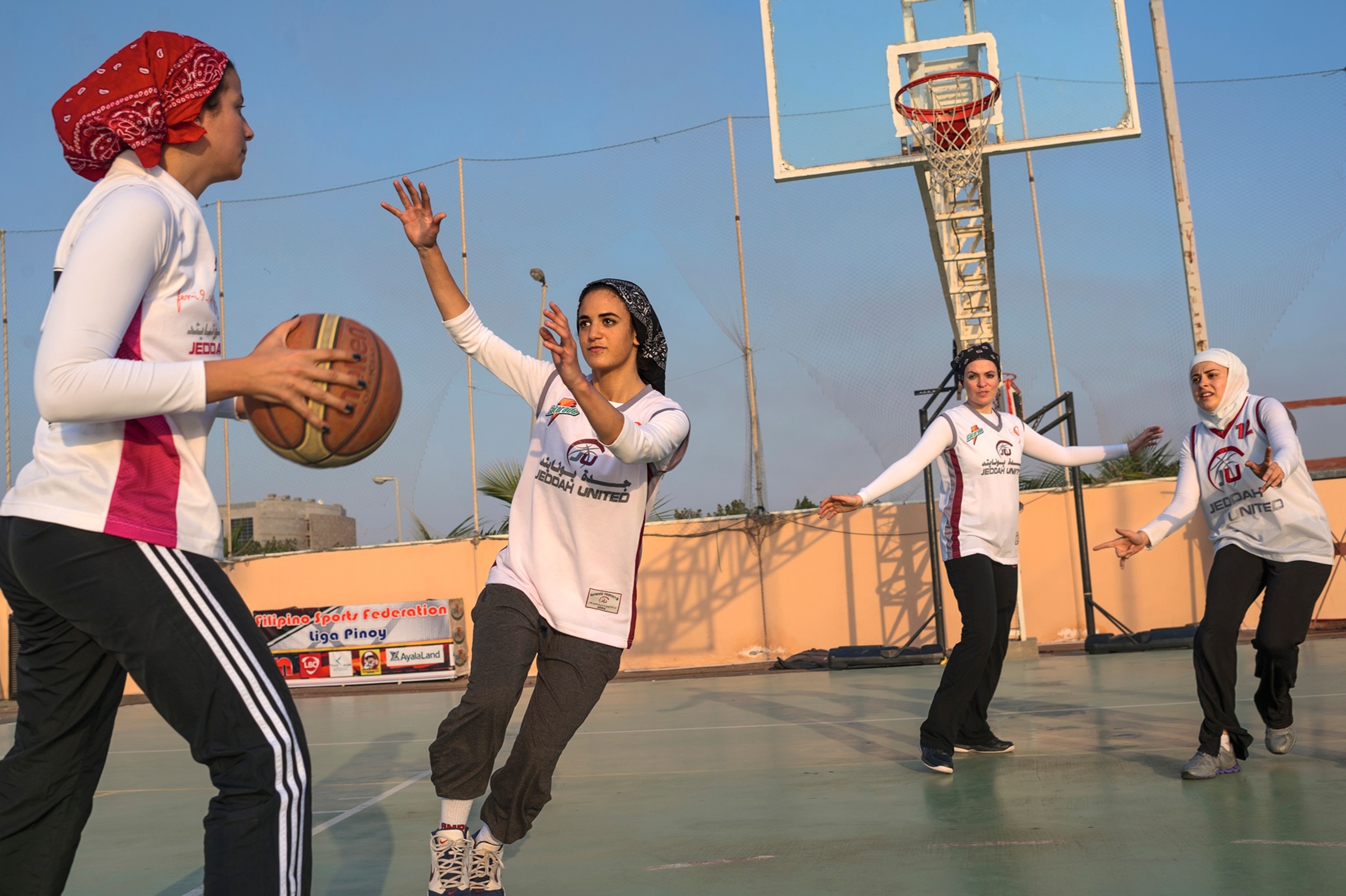 Four women with head coverings play basketball on a court.