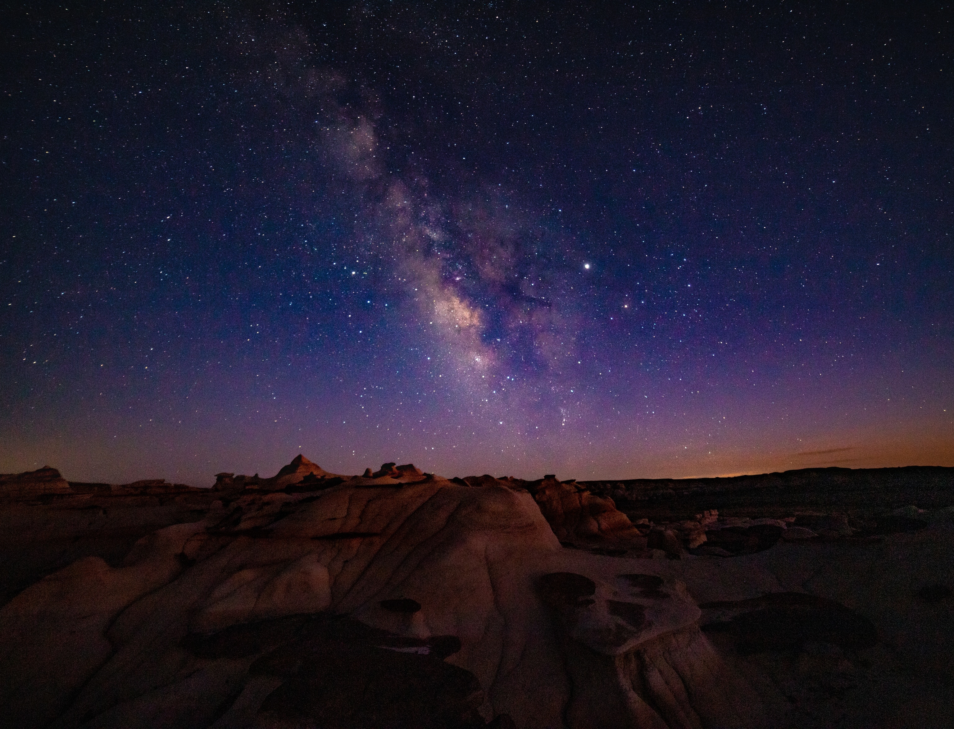 A vibrant night sky displays the Milky Way over sculpted desert rocks.