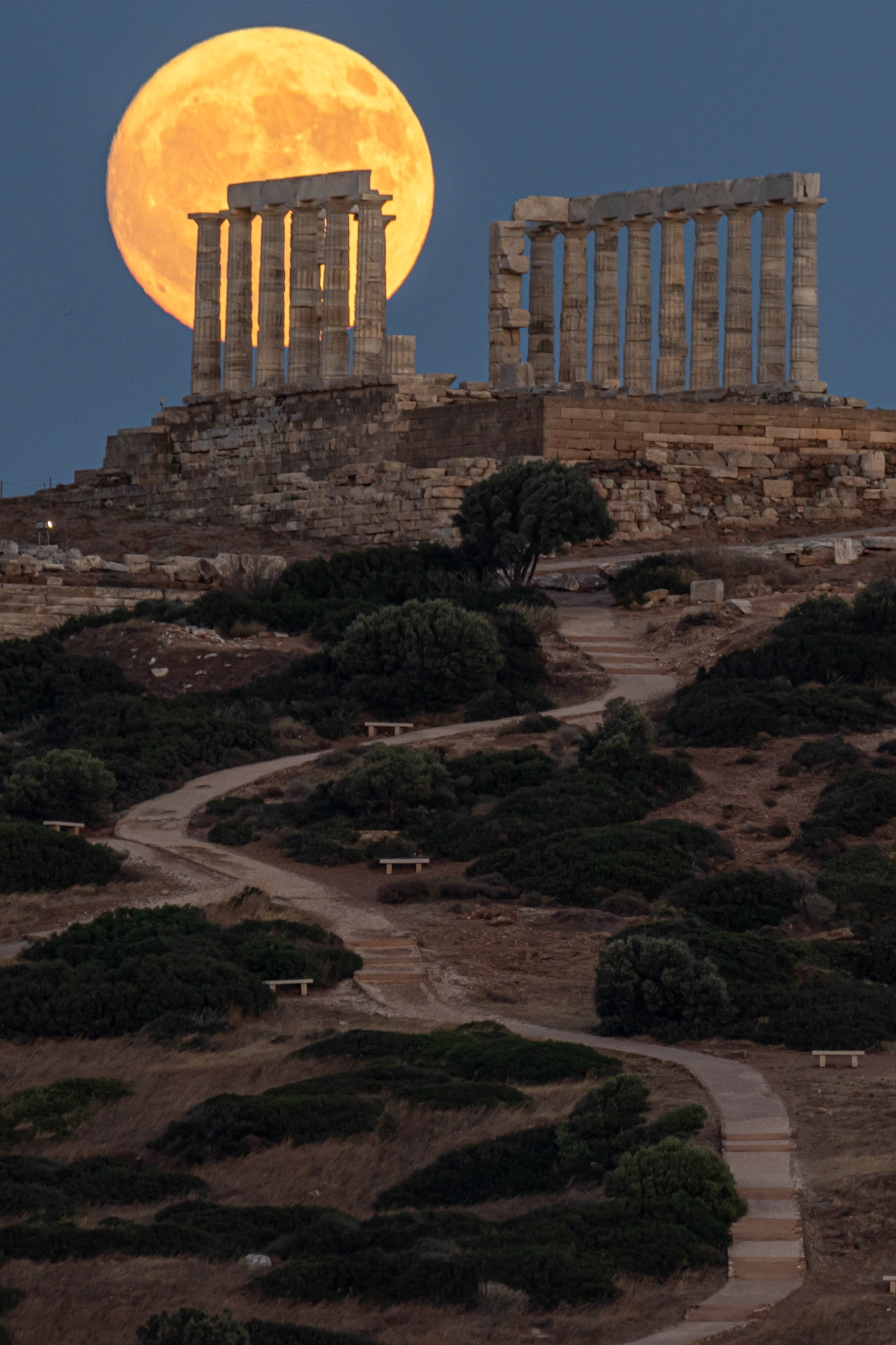 A glowing full moon rises behind the ancient ruins of a temple on a hill