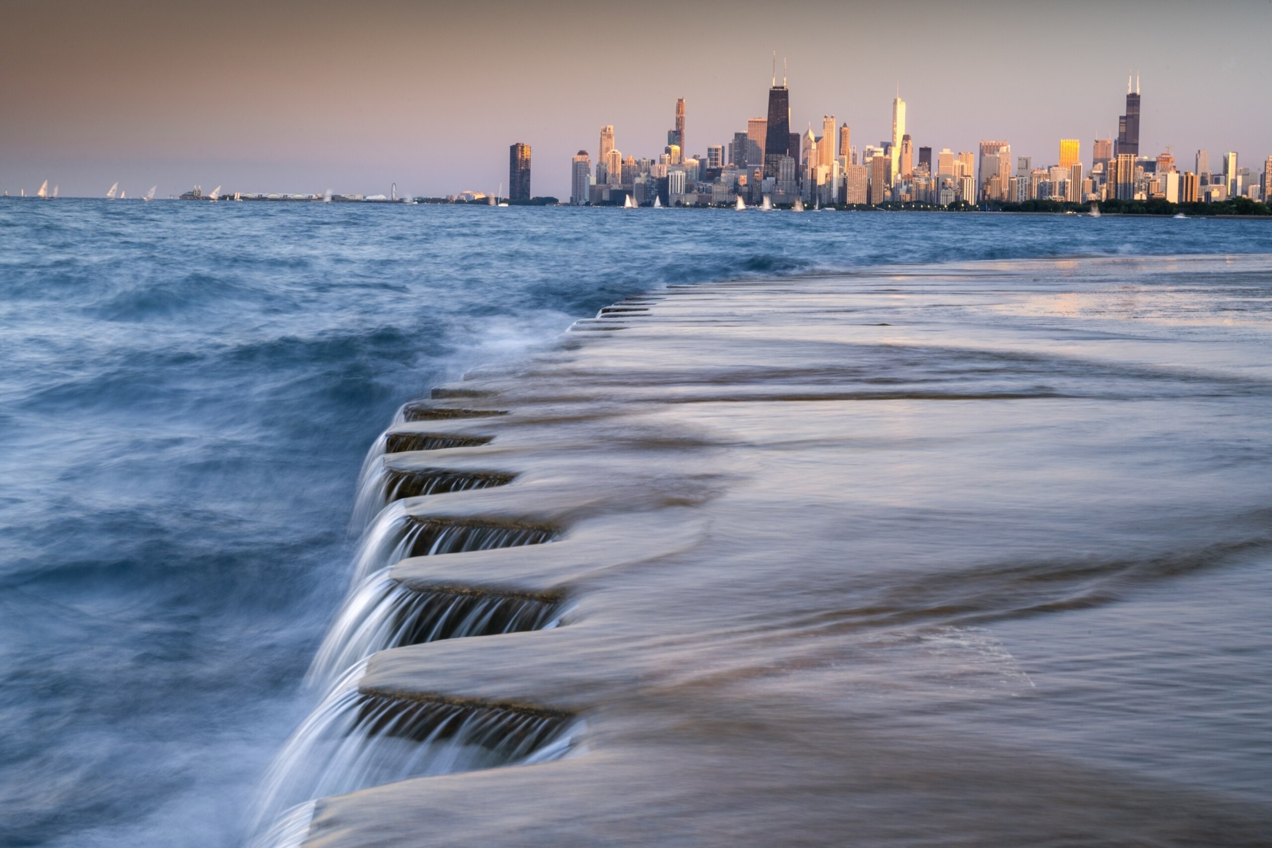 water running over the edge of walkway with a city on background.