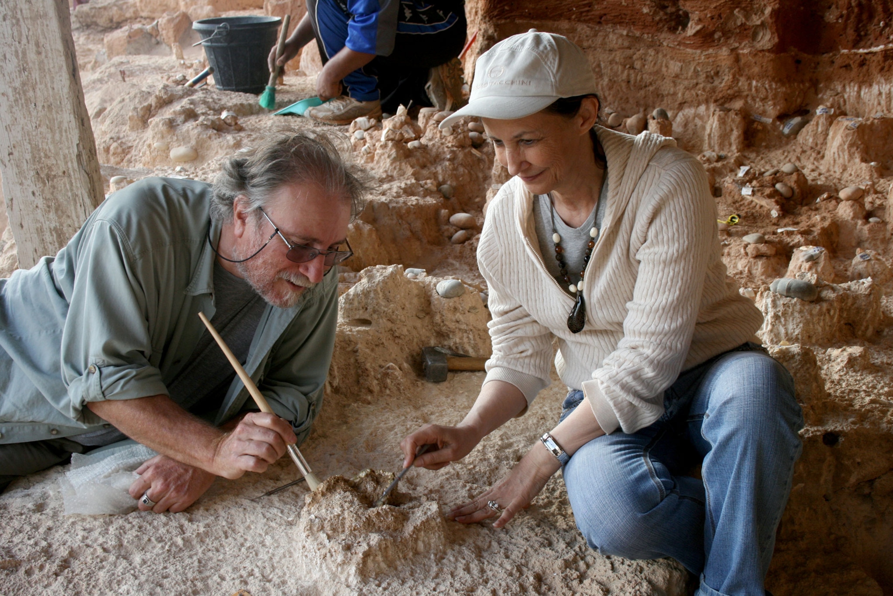 A man and woman with small brushes dusting dirt away.