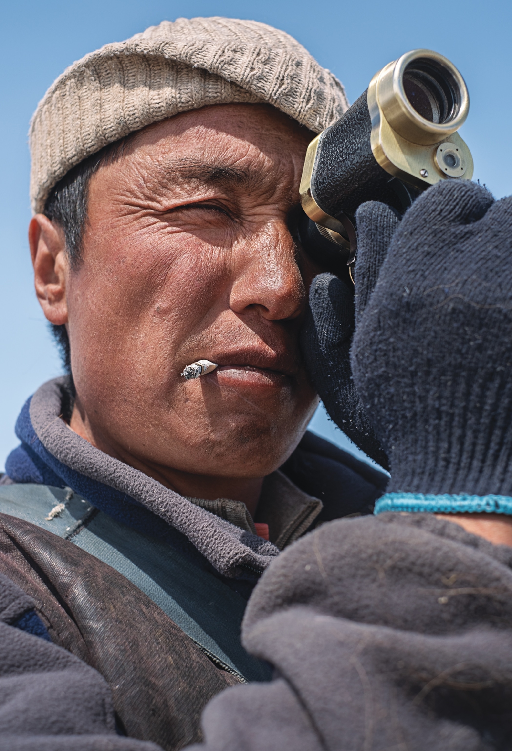 Man with cigaret in his lips looking through the functional lens of his binocular.