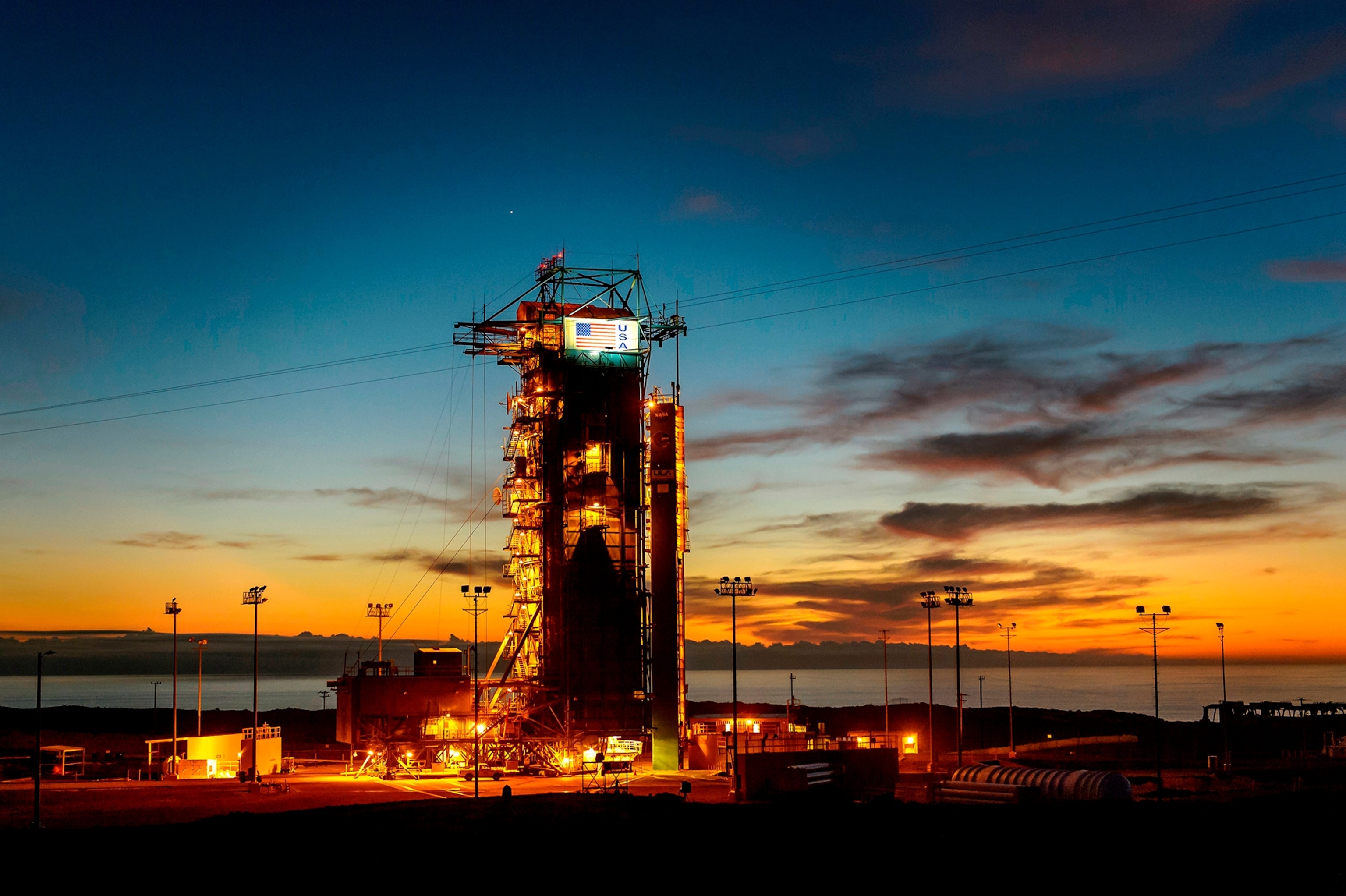 the sun sets behind Space Launch Complex 2 (SLC-2) with the Delta II rocket and the Soil Moisture Active Passive (SMAP) observatory protected by the service structure on Tuesday, Jan. 27, 2015, at Vandenberg Air Force Base, Calif.