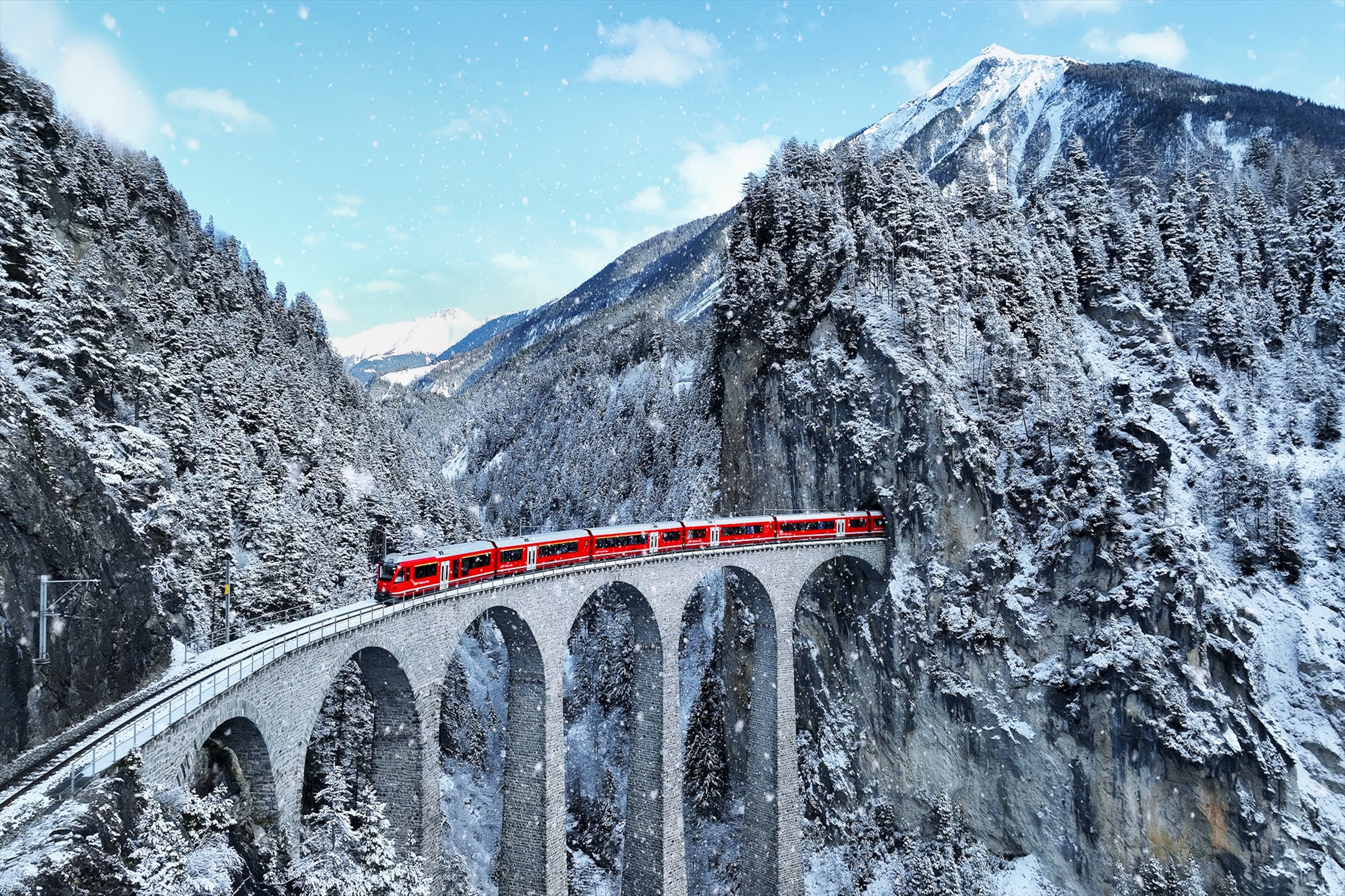 A red and white train curves around a bridge in the winter in Switzerland.