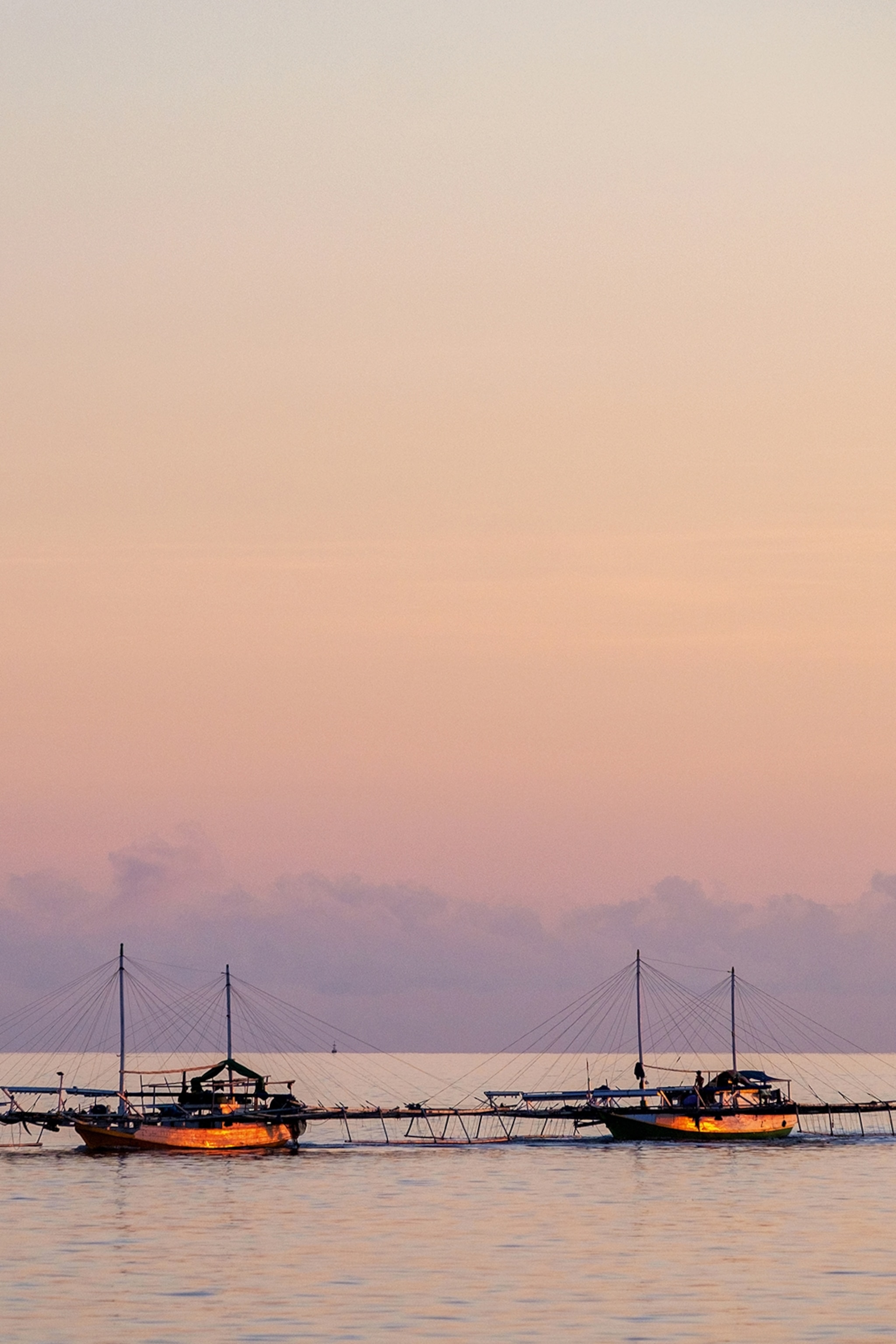 A couple of fishing boats docked at a free-standing pier in the middle of the ocean at sunset.