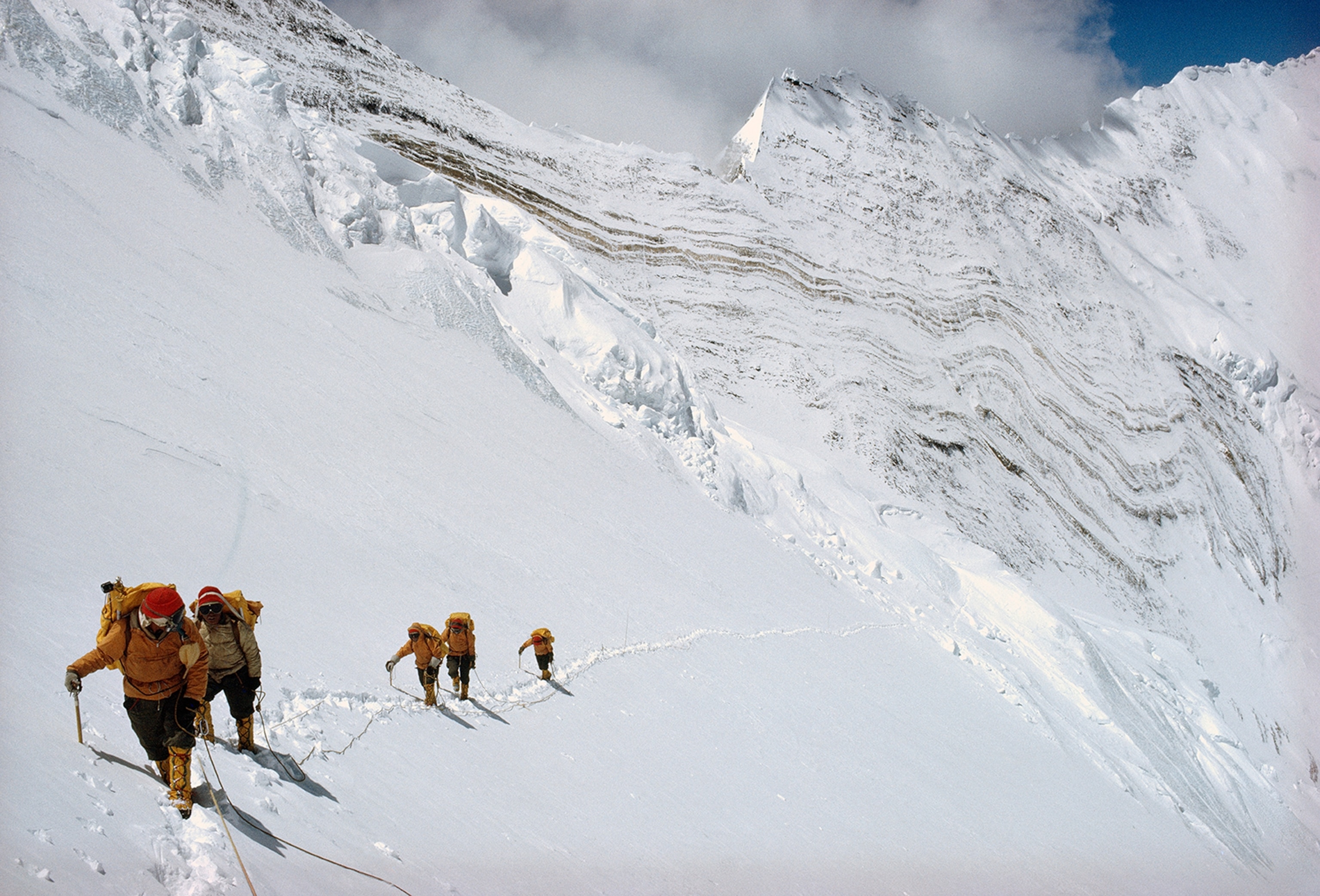 Writhing limestone layers beneath the saw-tooth ridge connecting Lhotse and Nuptse form the famous Yellow Band. Roped together, climbers toil up Lhotse’s face with supplies for Camp V in the South Col.