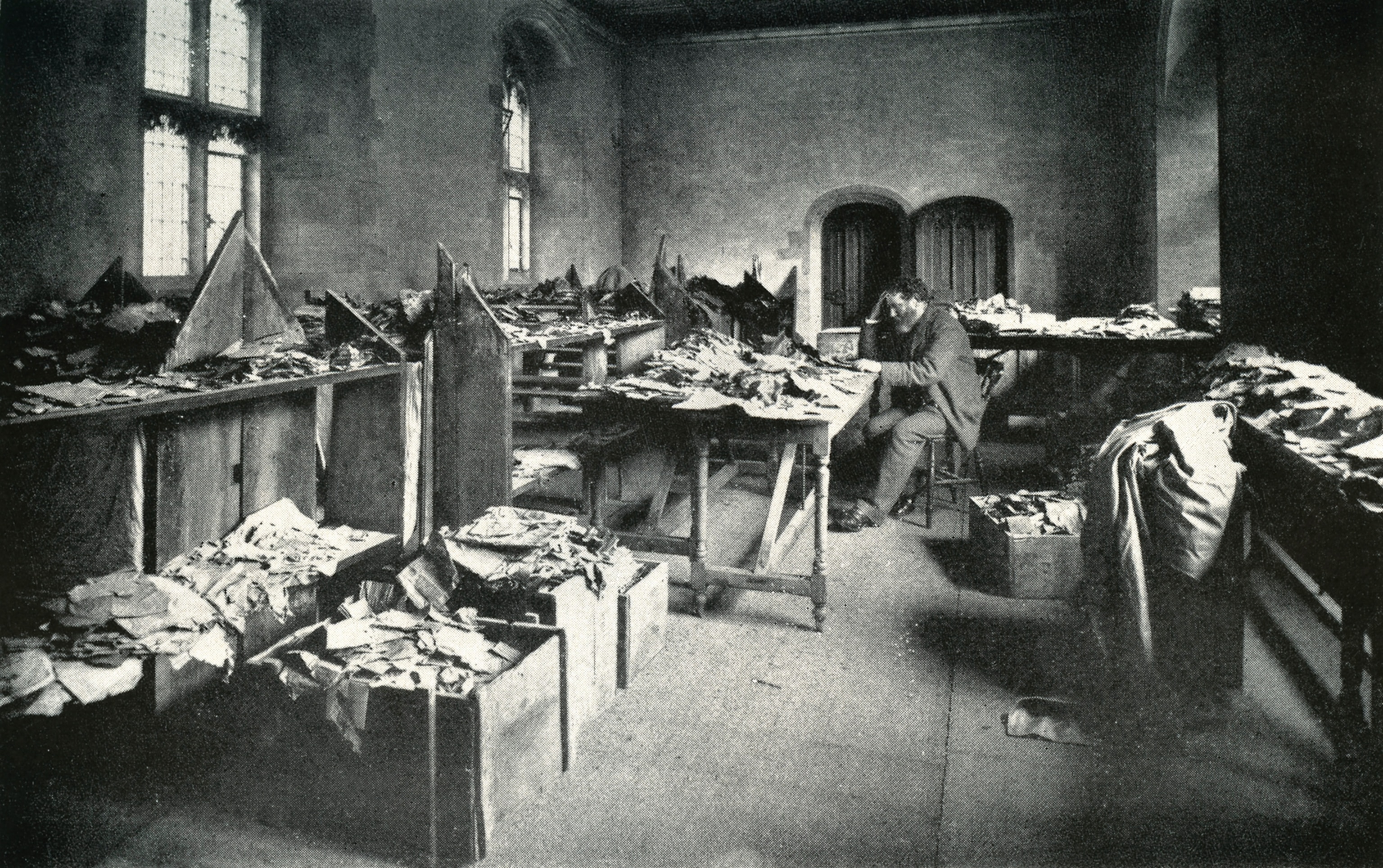 Photograph of Solomon Schechter surrounded by boxes overflowing with manuscripts.