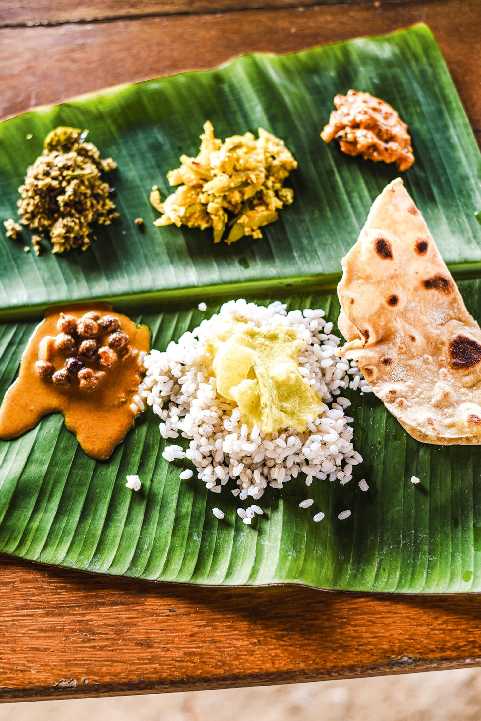 A banana leaf used as a plate containing multiple small portions of spiced vegetables, rice and chapati.