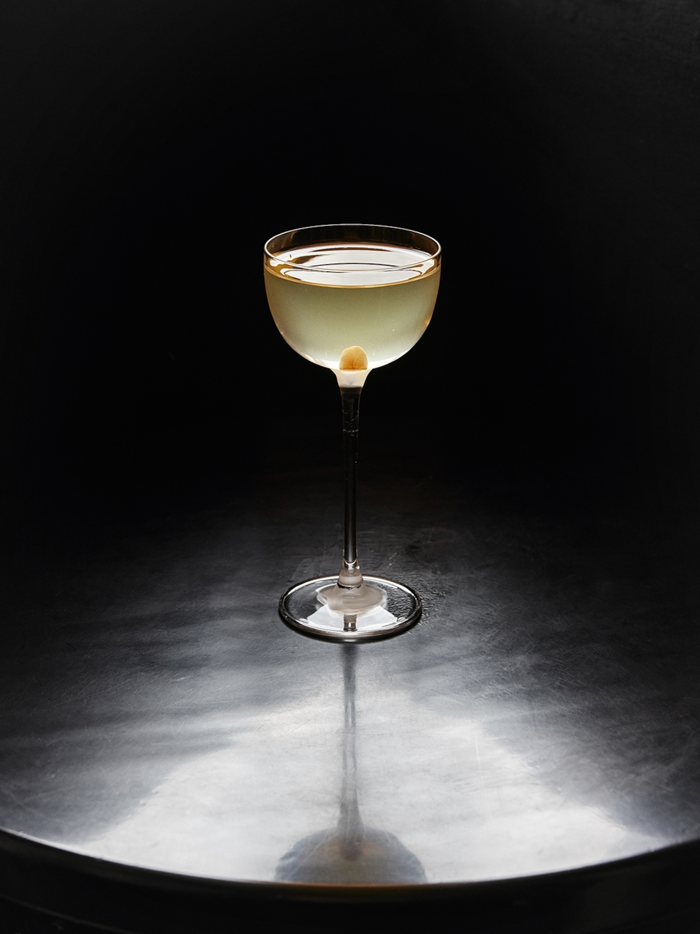 A cocktail glass on a table in spotlighting.