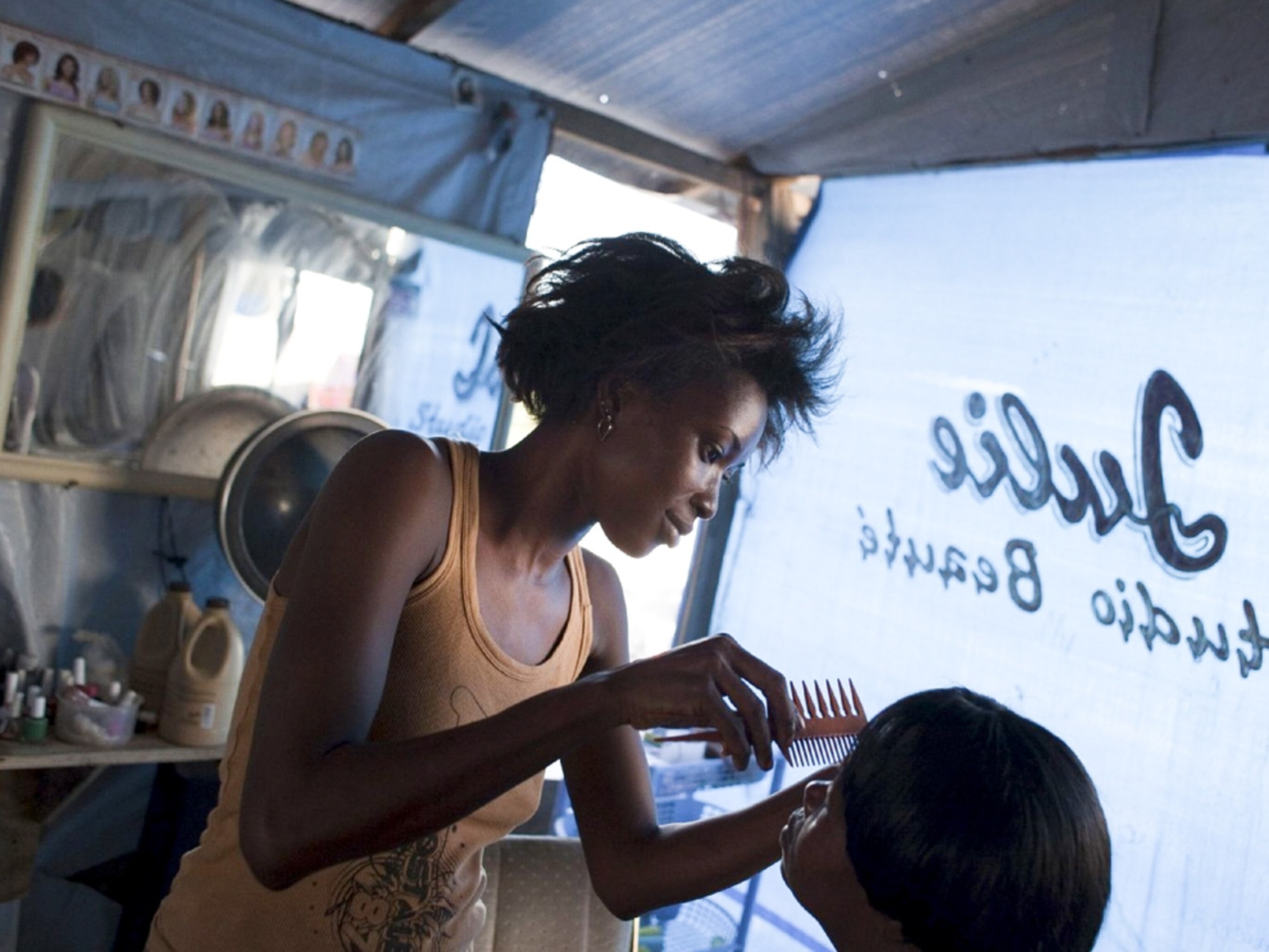 A Haitian woman weaves hair in a refugee camp hair salon -- picture from a photo gallery on the one-year Haiti-earthquake anniversary