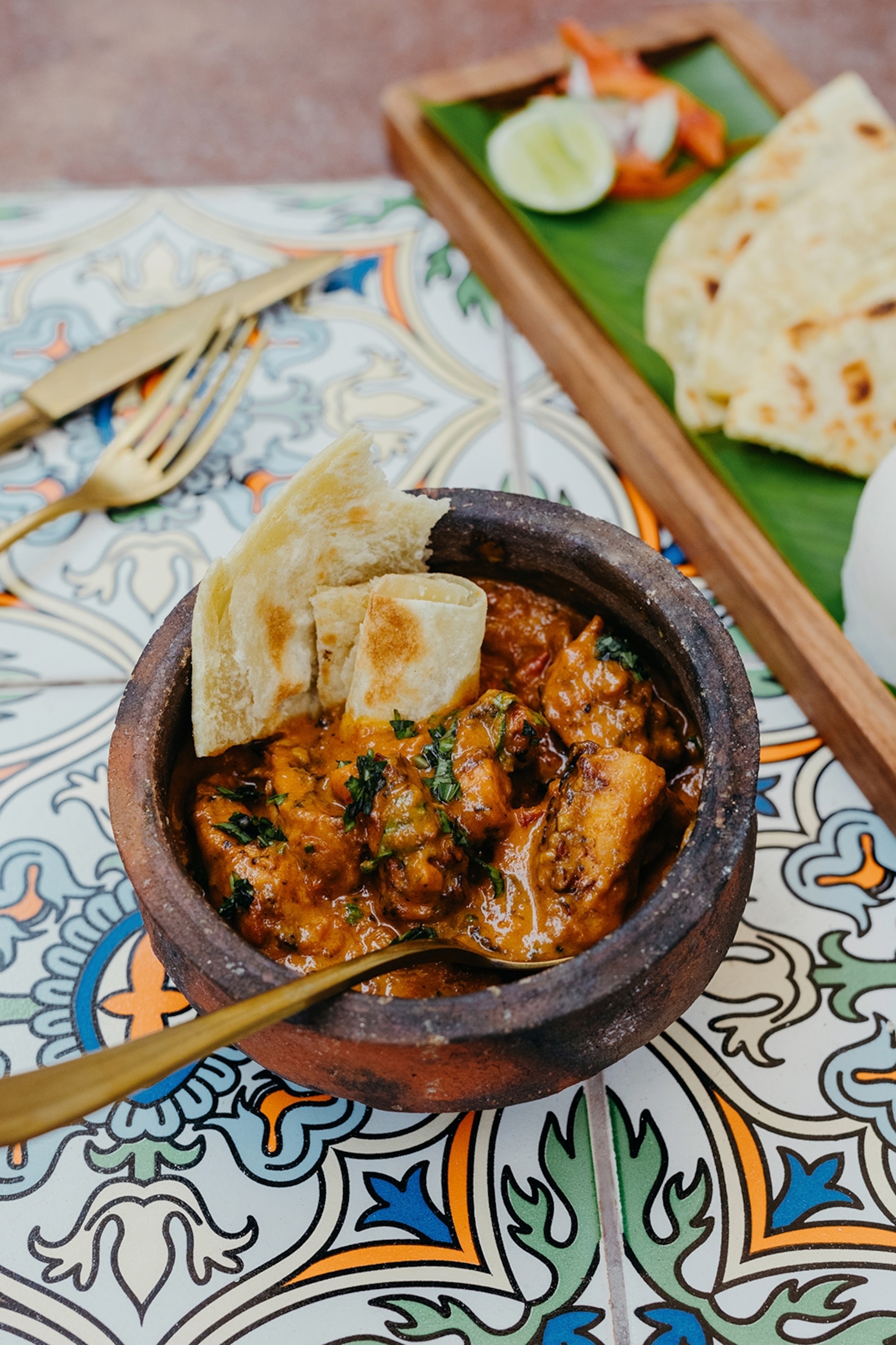 A bowl of spiced curry on a patterned table cloth served with slices of bread.