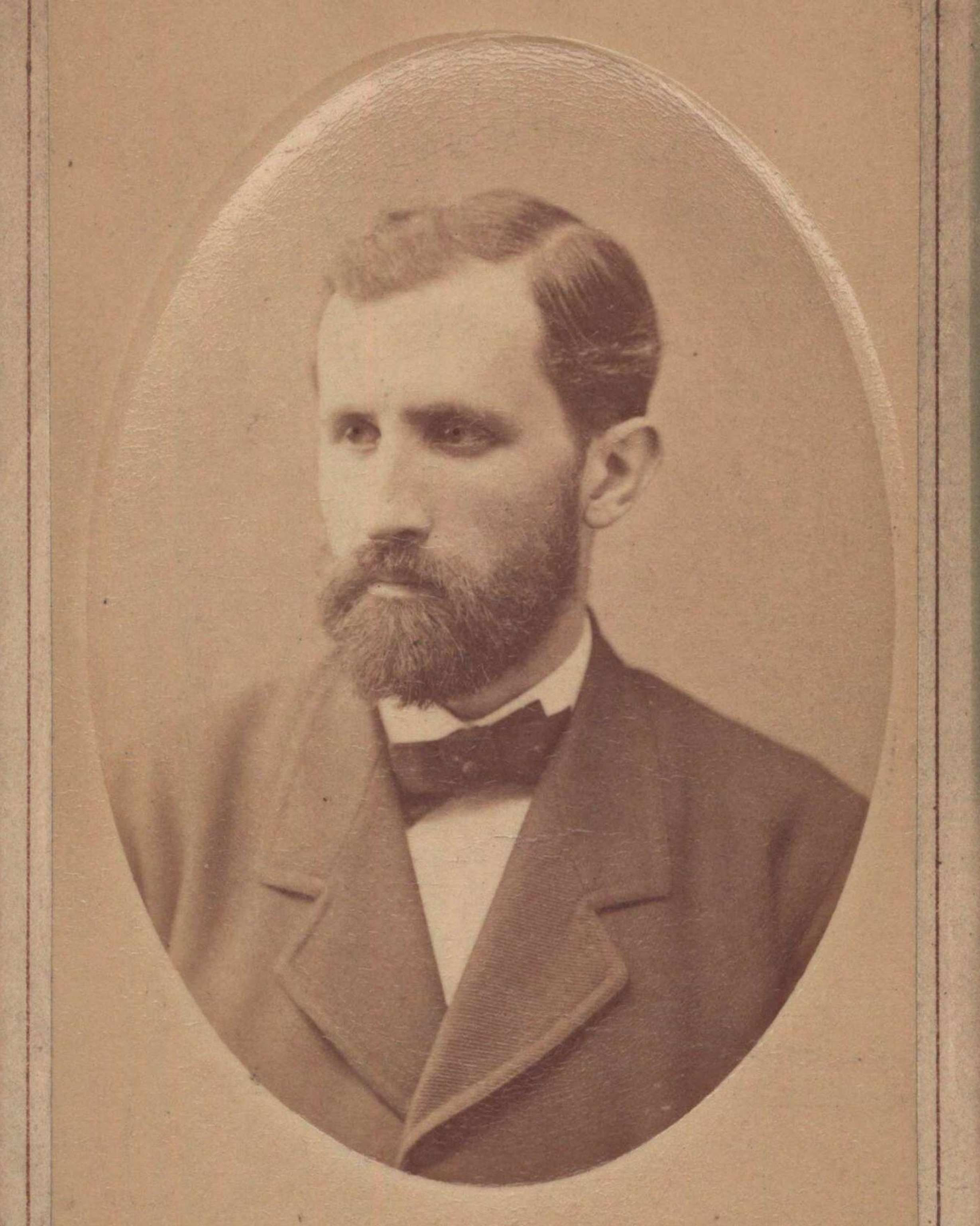 Sepia-toned portrait of a bearded man in a suit and bow tie, with a serious expression, framed in an oval.