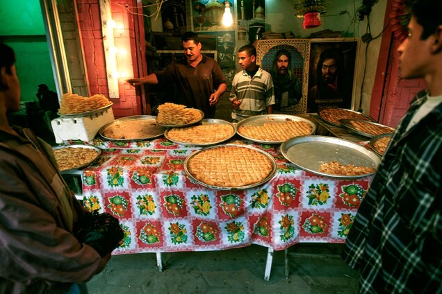 Men sell pastries displayed on a street side table prior to Iftar.