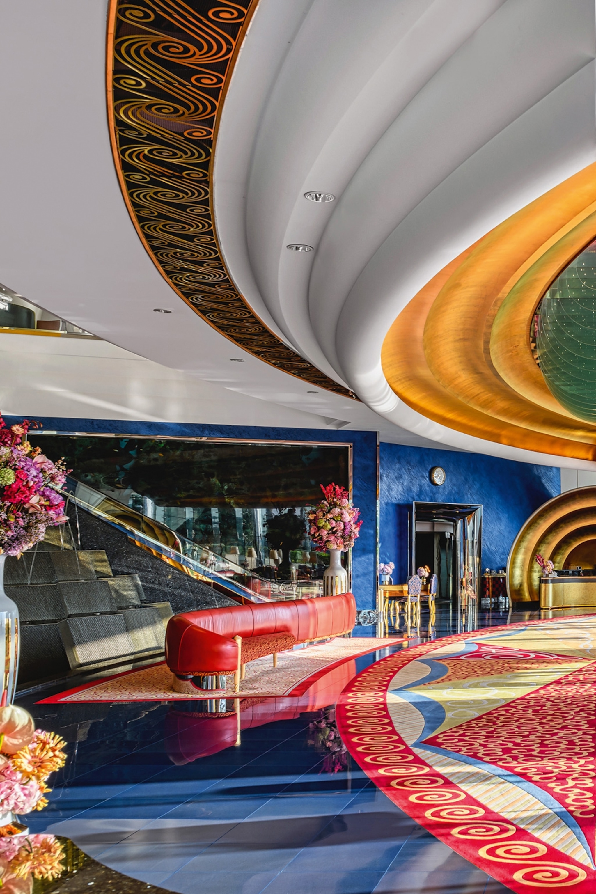 A tiles and spacious lobby with a symmetrical gemstone ceiling and gold frames on stairs, sofas and room corners.