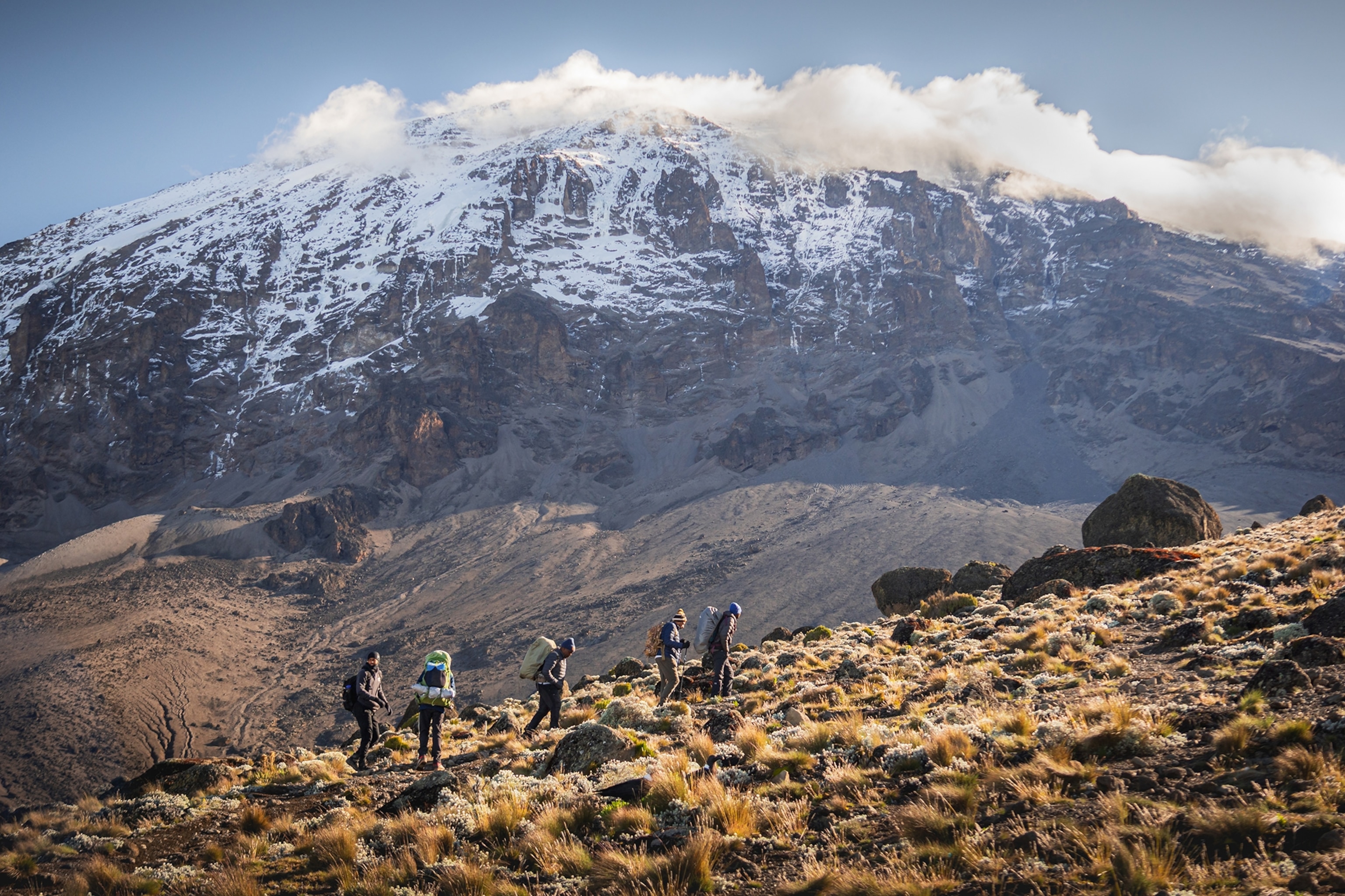 A impressive mountain landscape shot showing a group of hikers trekking up the bushy slopes of a mountain.