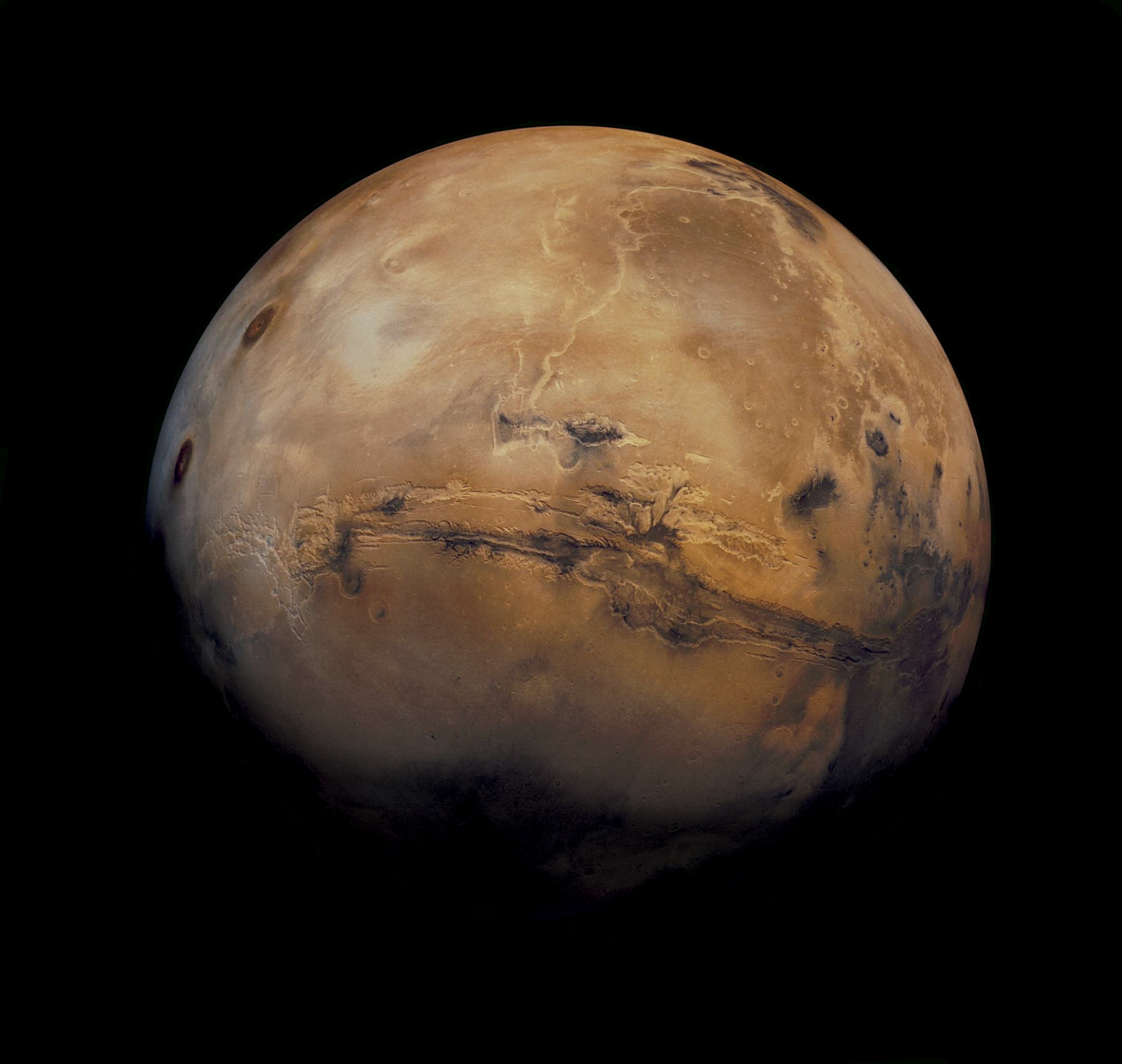 A detailed view of Mars against a black background, showcasing its reddish surface with craters and a large canyon system