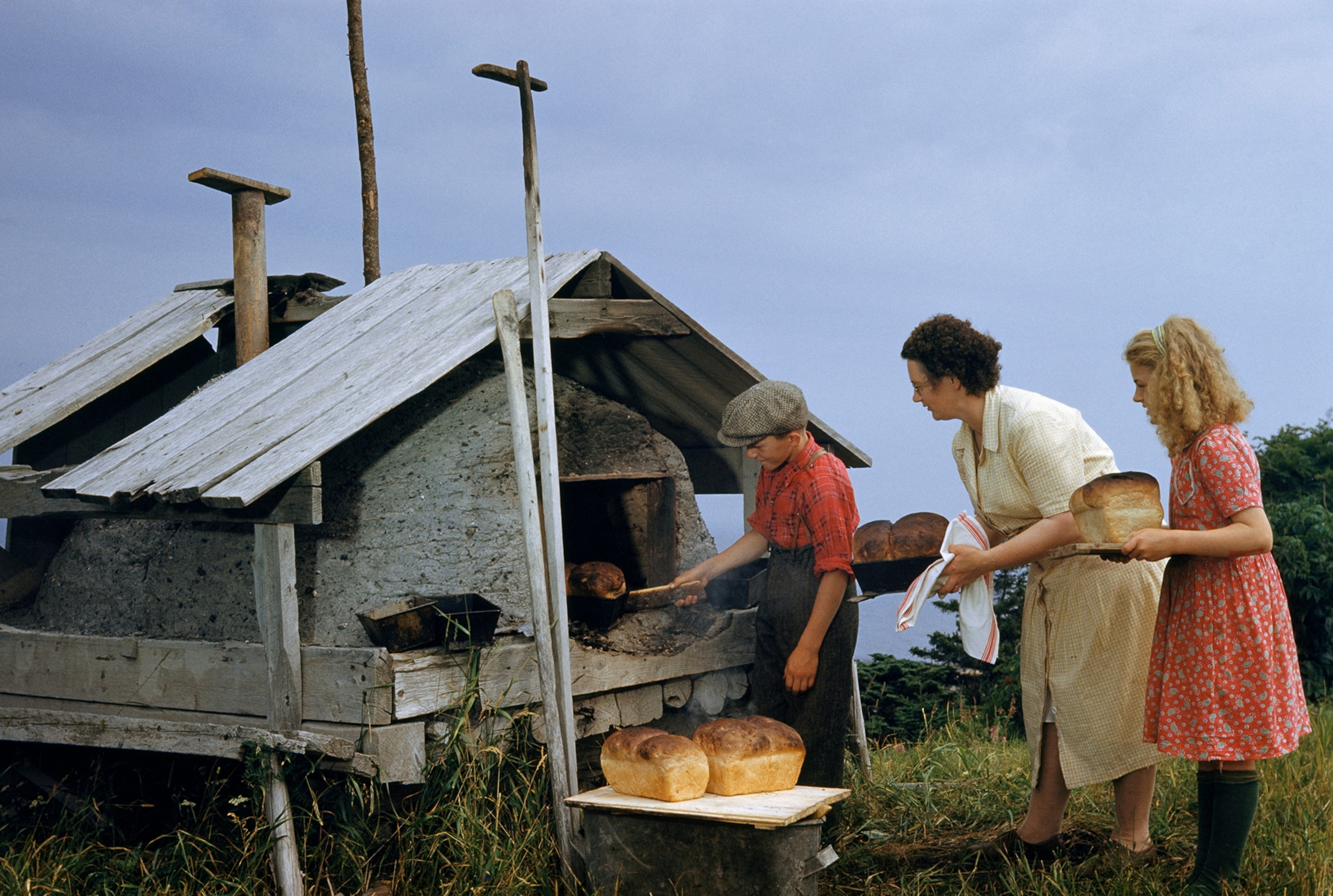 a mother and her children lift the week's bread from an outdoor oven