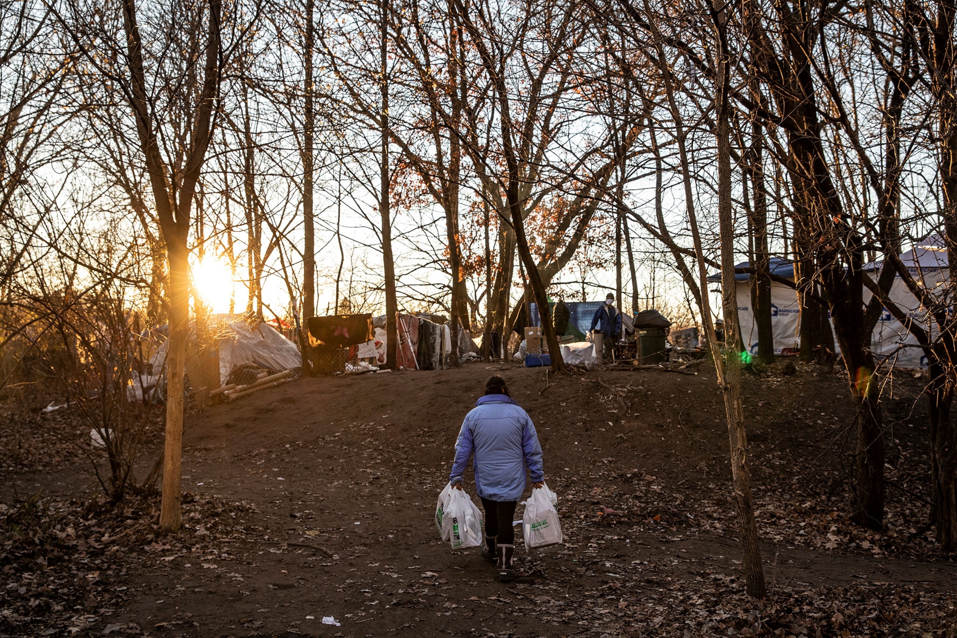 Homeless person walks back to her city park tent with food in hand.