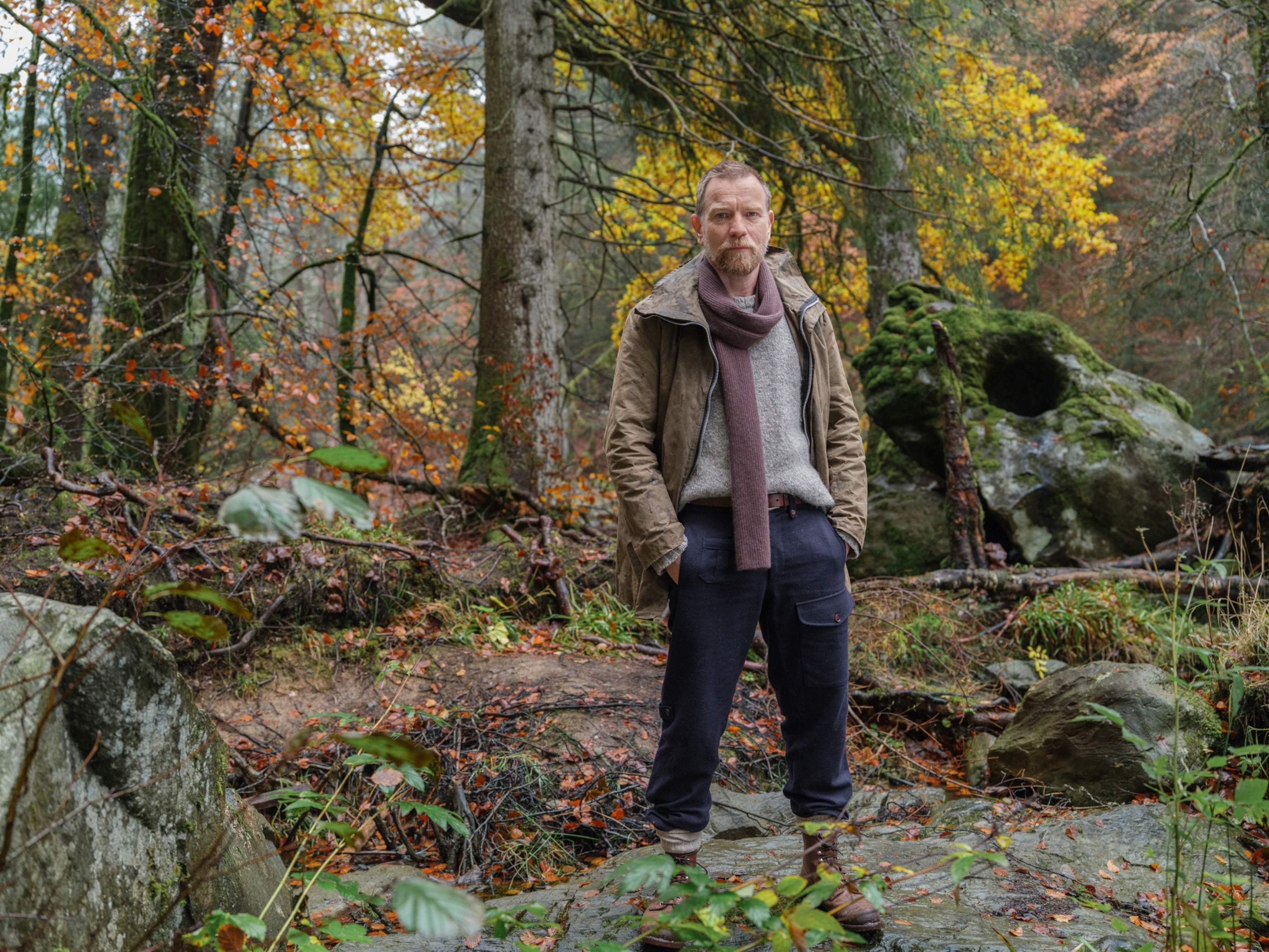 A man stands among a green forest.