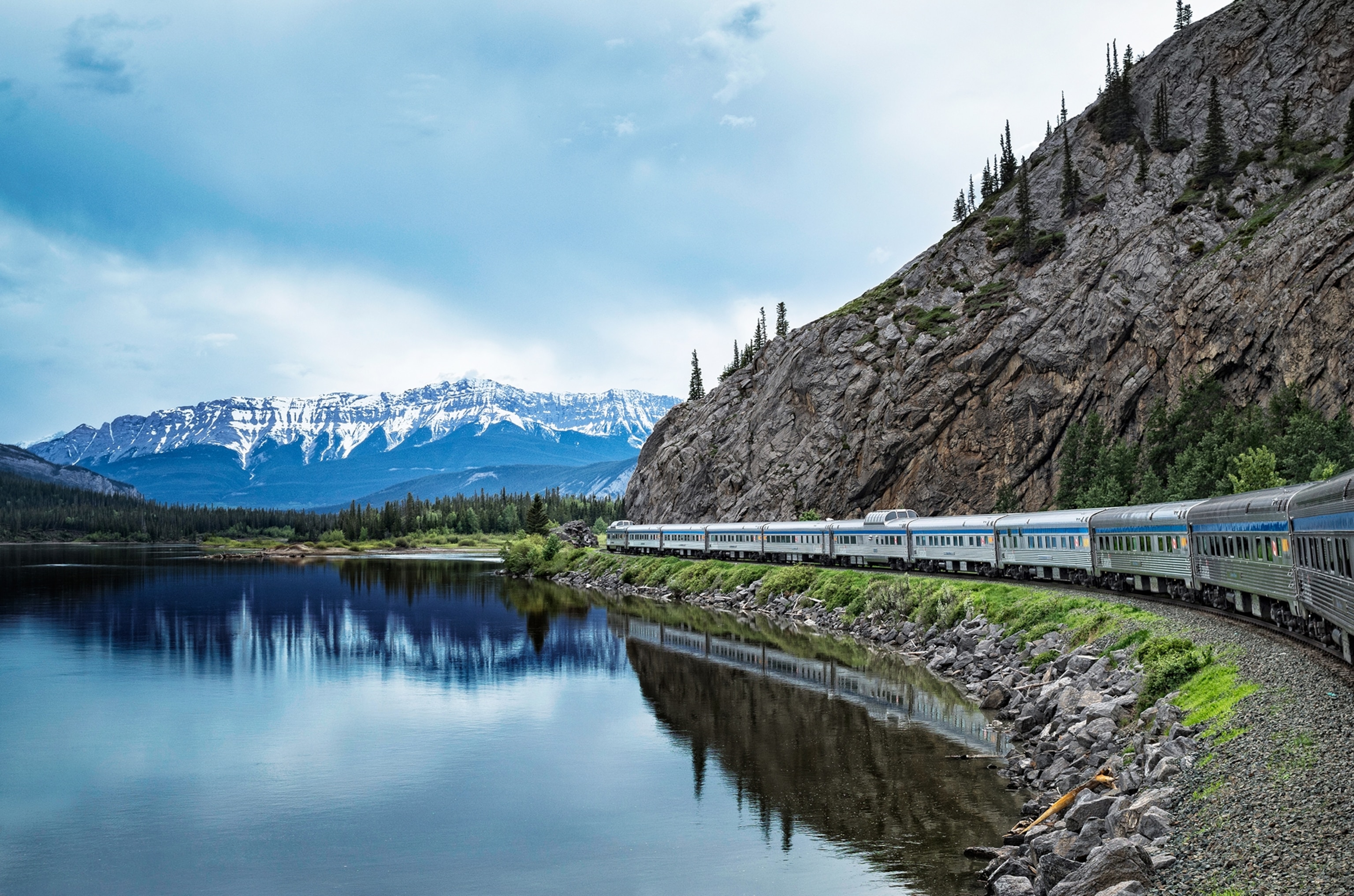 A silver train travels through a mountainous landscape