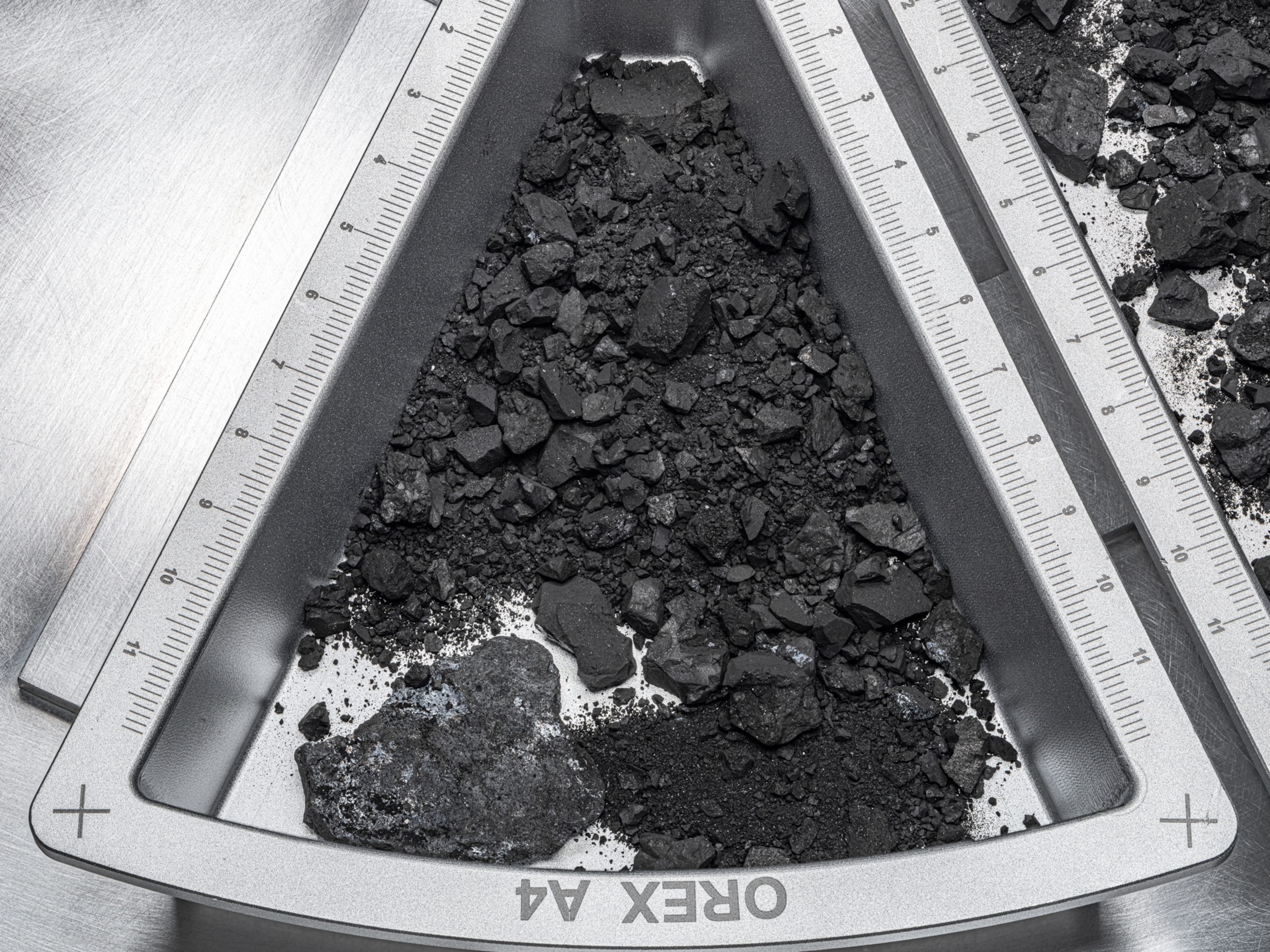 Close-up of a metallic container holding dark samples of asteroid dust and rock.