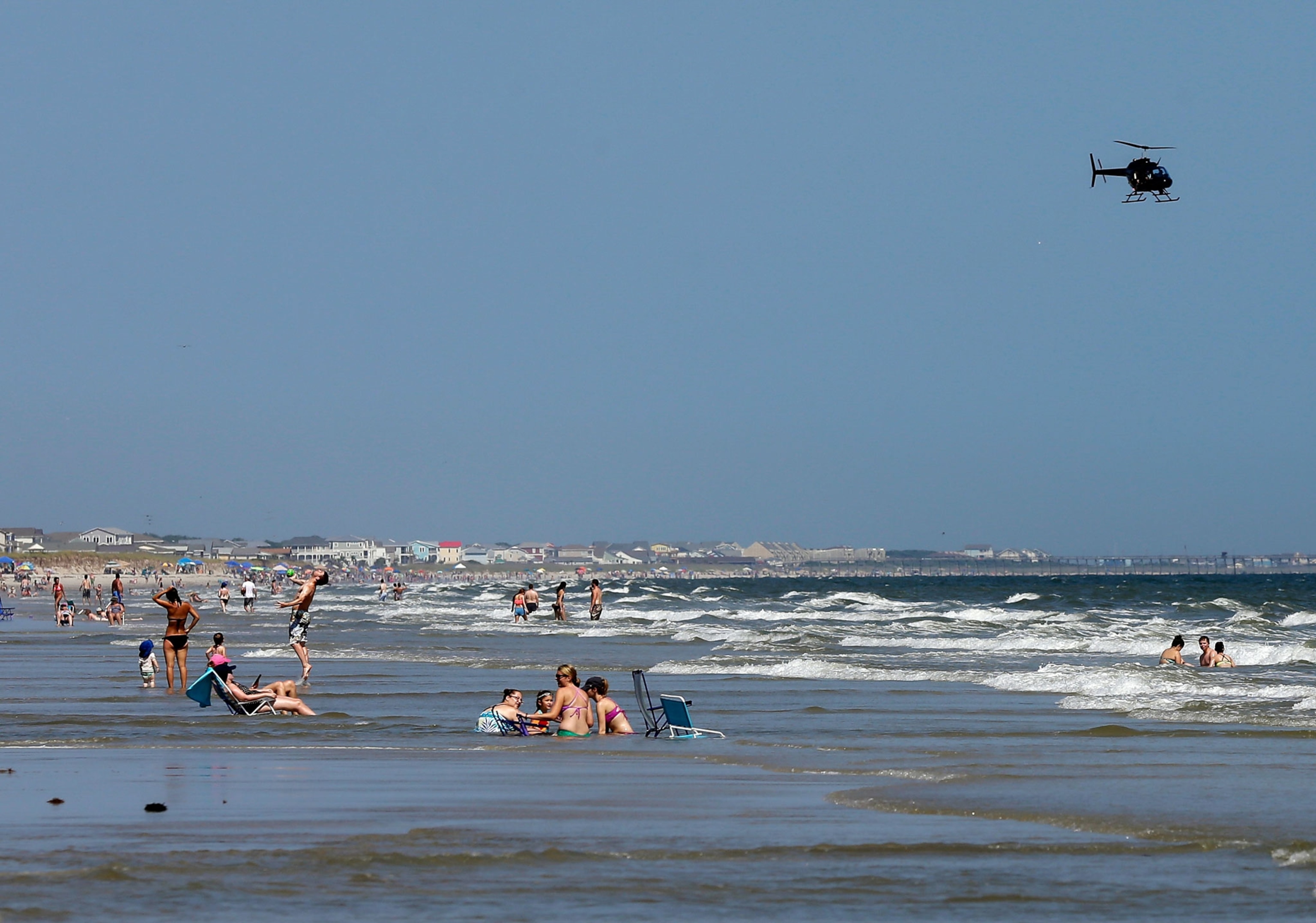 people on a beach in North Carolina while a helicopter patrols above